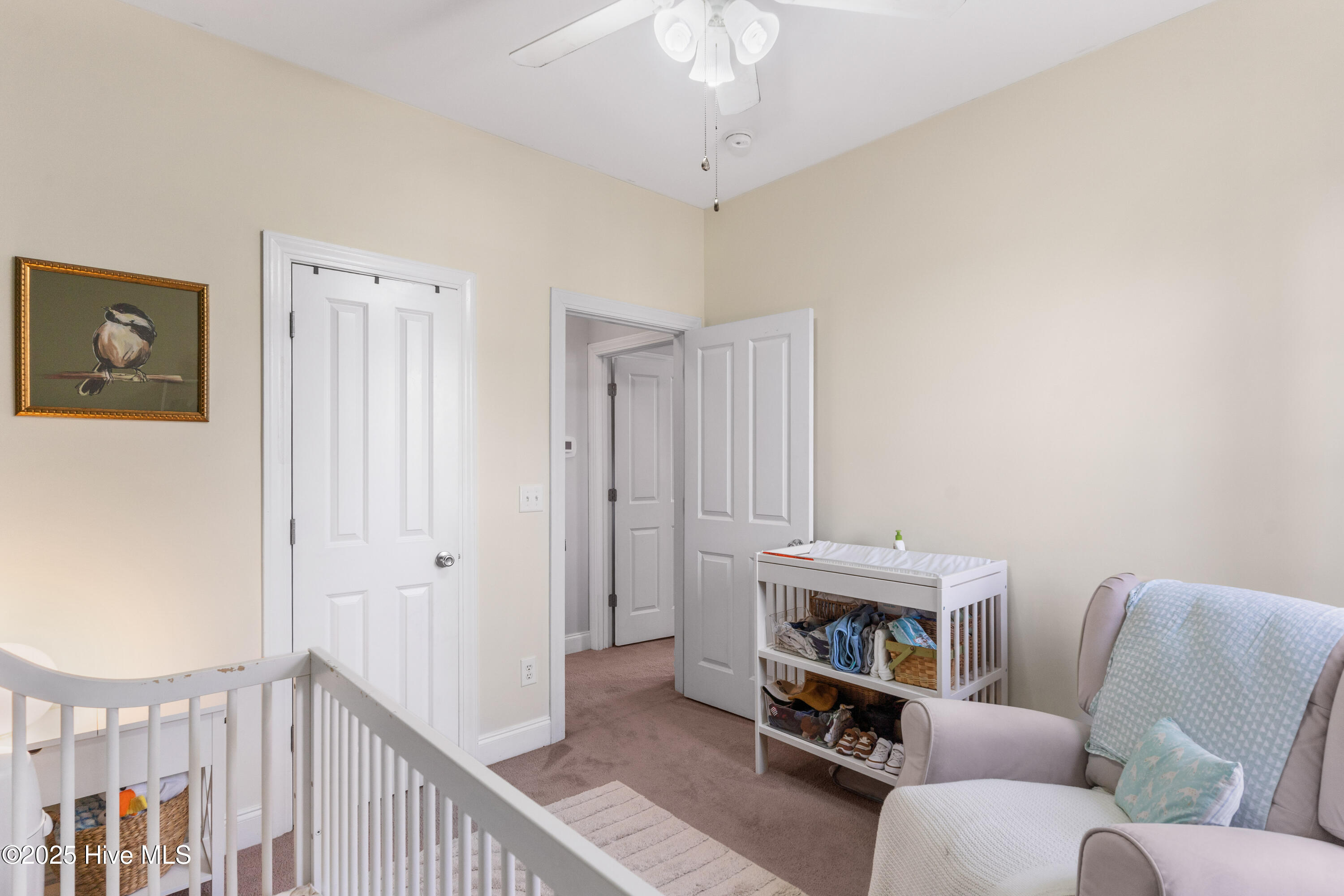 Nursery with a white crib, cushioned rocking chair, and shelving stocked with baby supplies.
