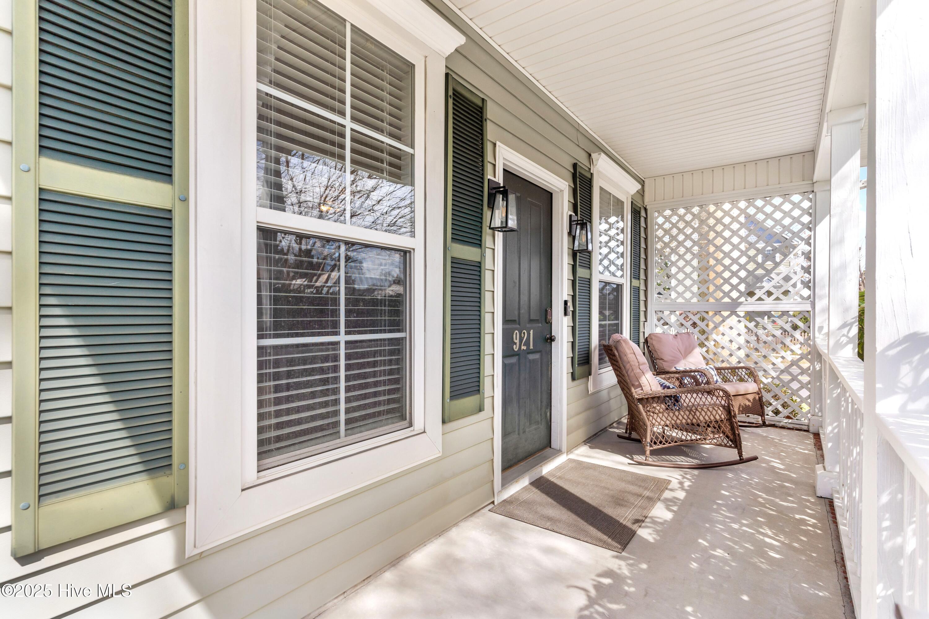 Covered front porch with green shutters, white lattice, and wicker rocking chairs.