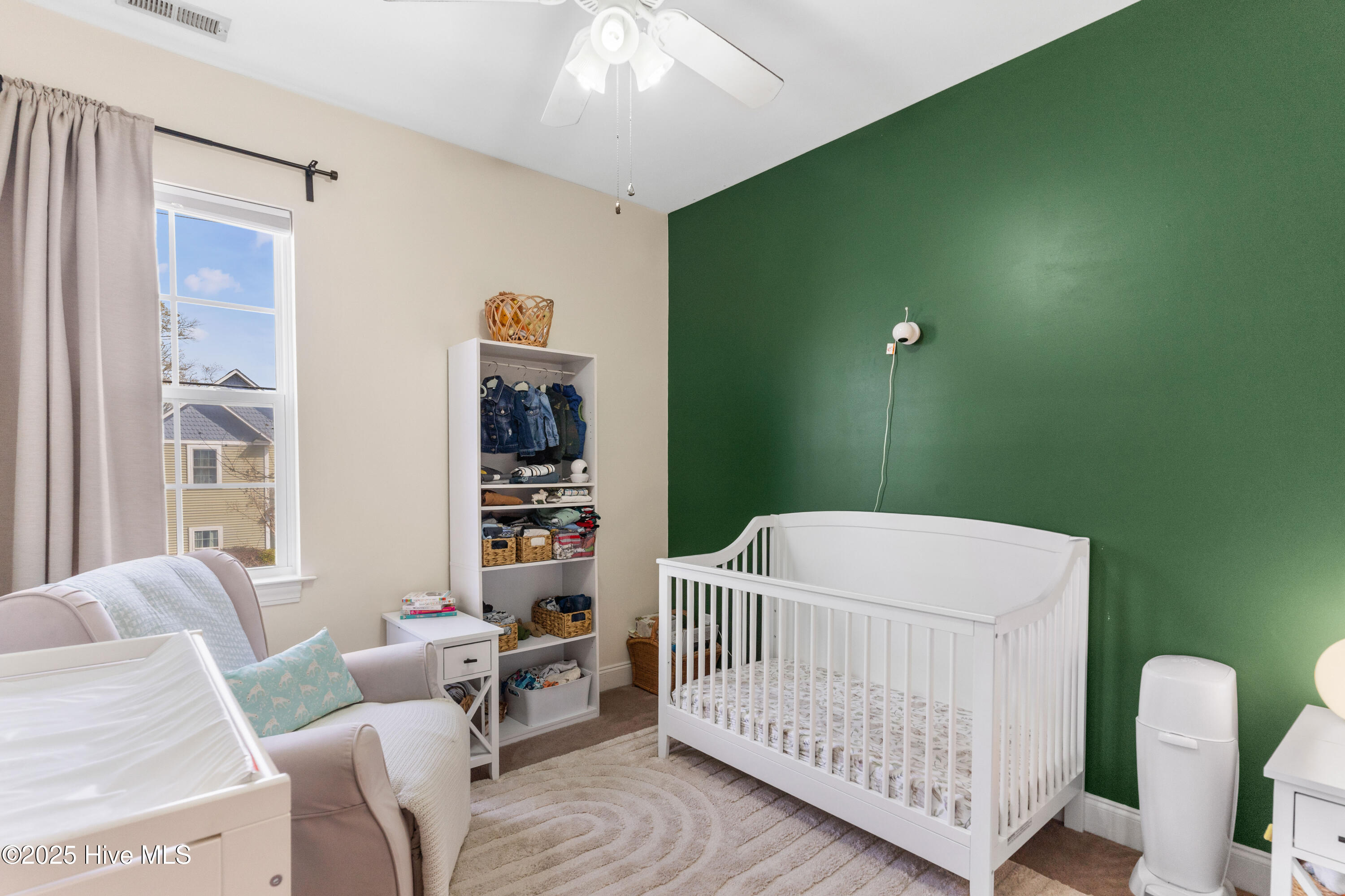 Nursery with a white crib, green accent wall, glider, and window.