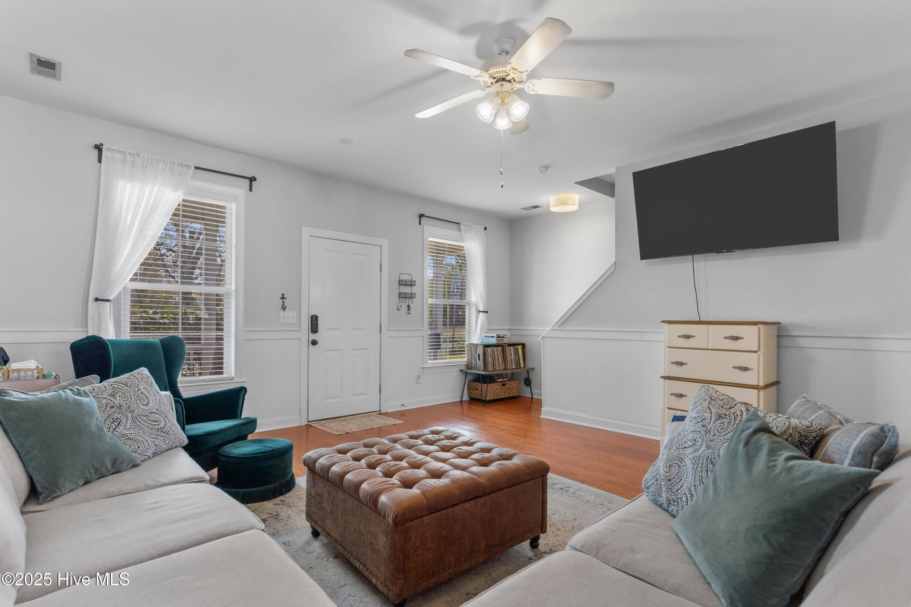 Furnished living room with a tufted leather ottoman, teal armchair, and wall-mounted television.