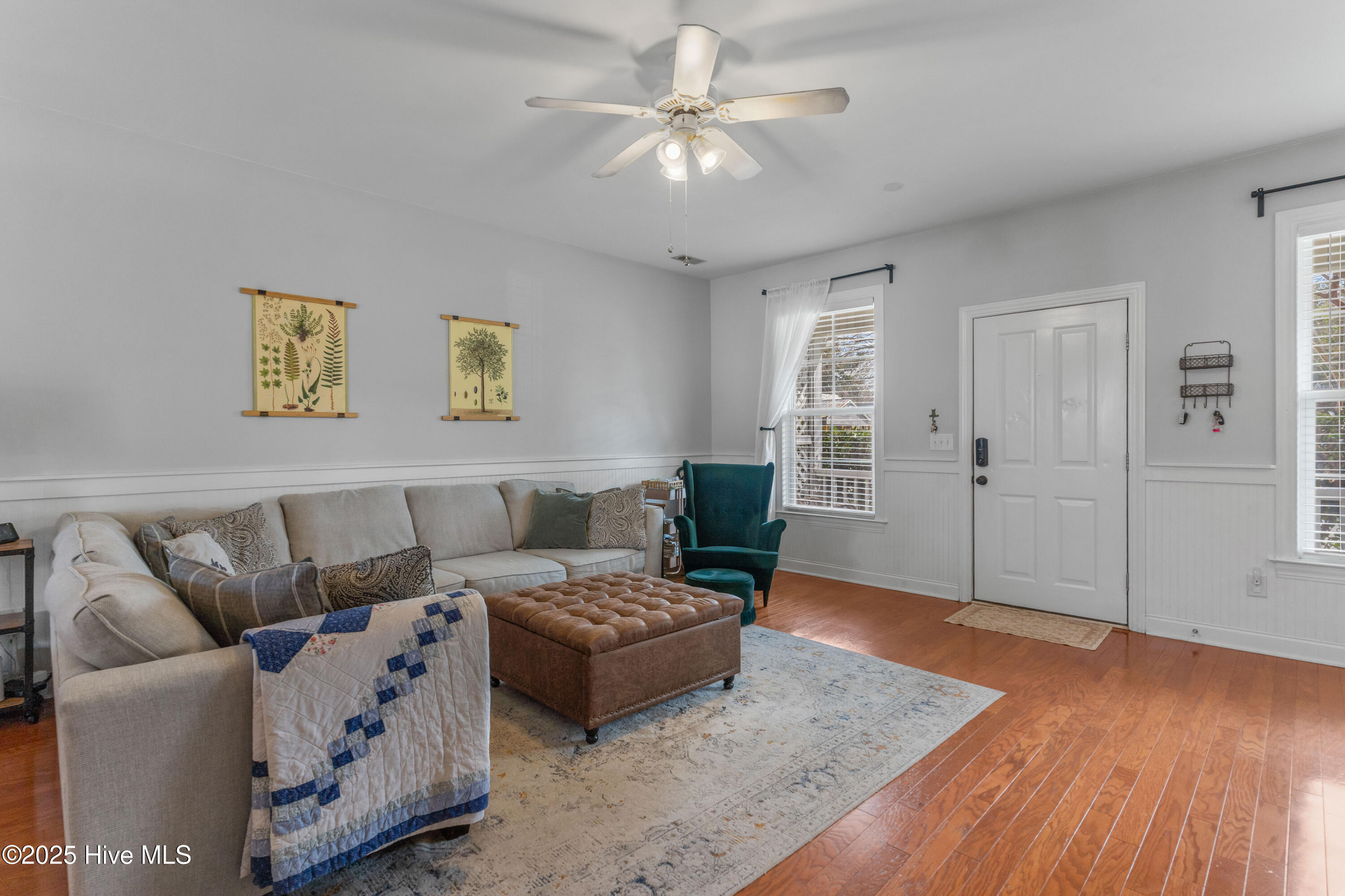Living room with a beige sectional, brown tufted ottoman, teal armchair, and hardwood floors.