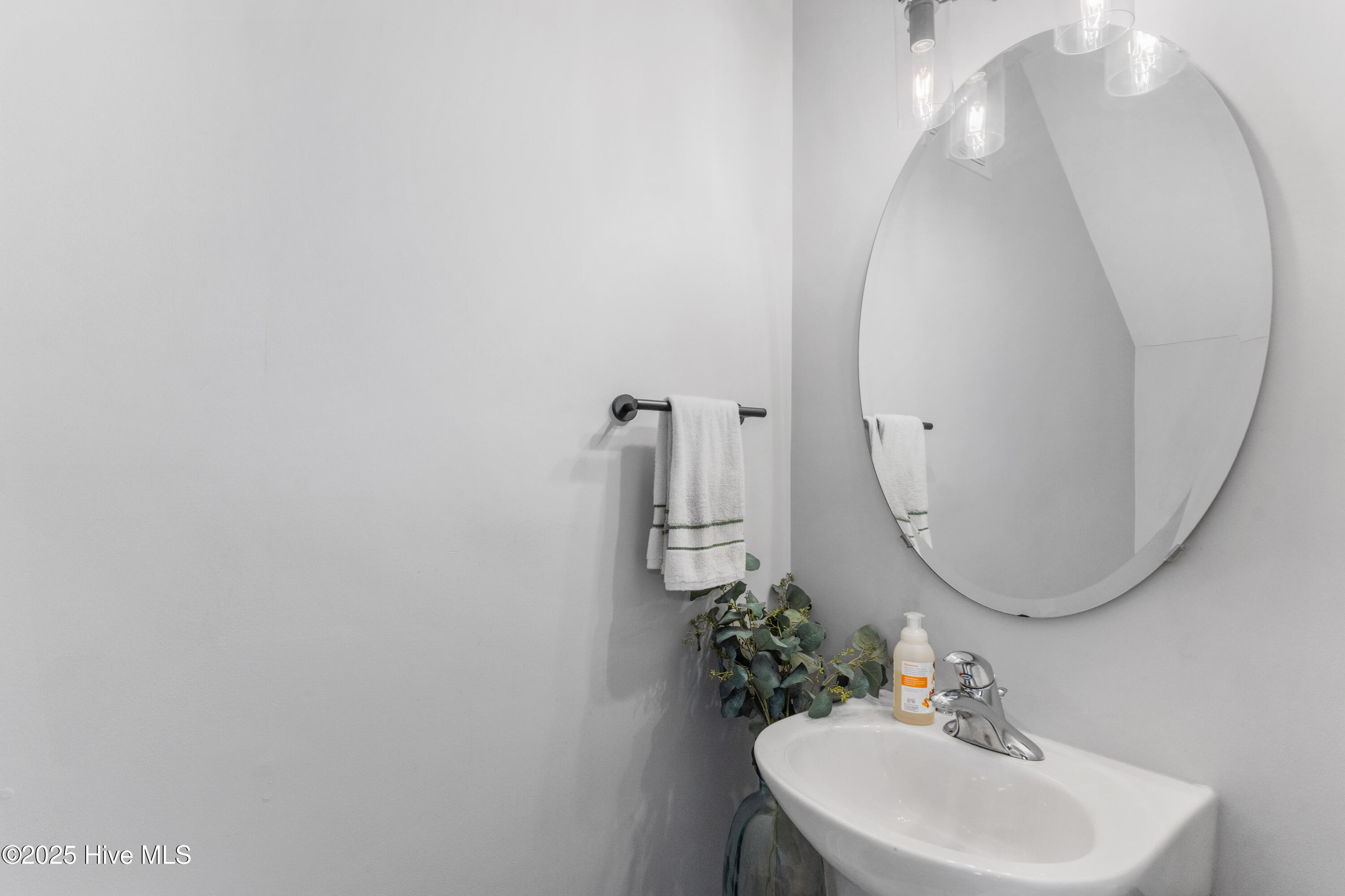 Bathroom sink and chrome faucet beneath a large oval mirror, with striped towels and greenery.