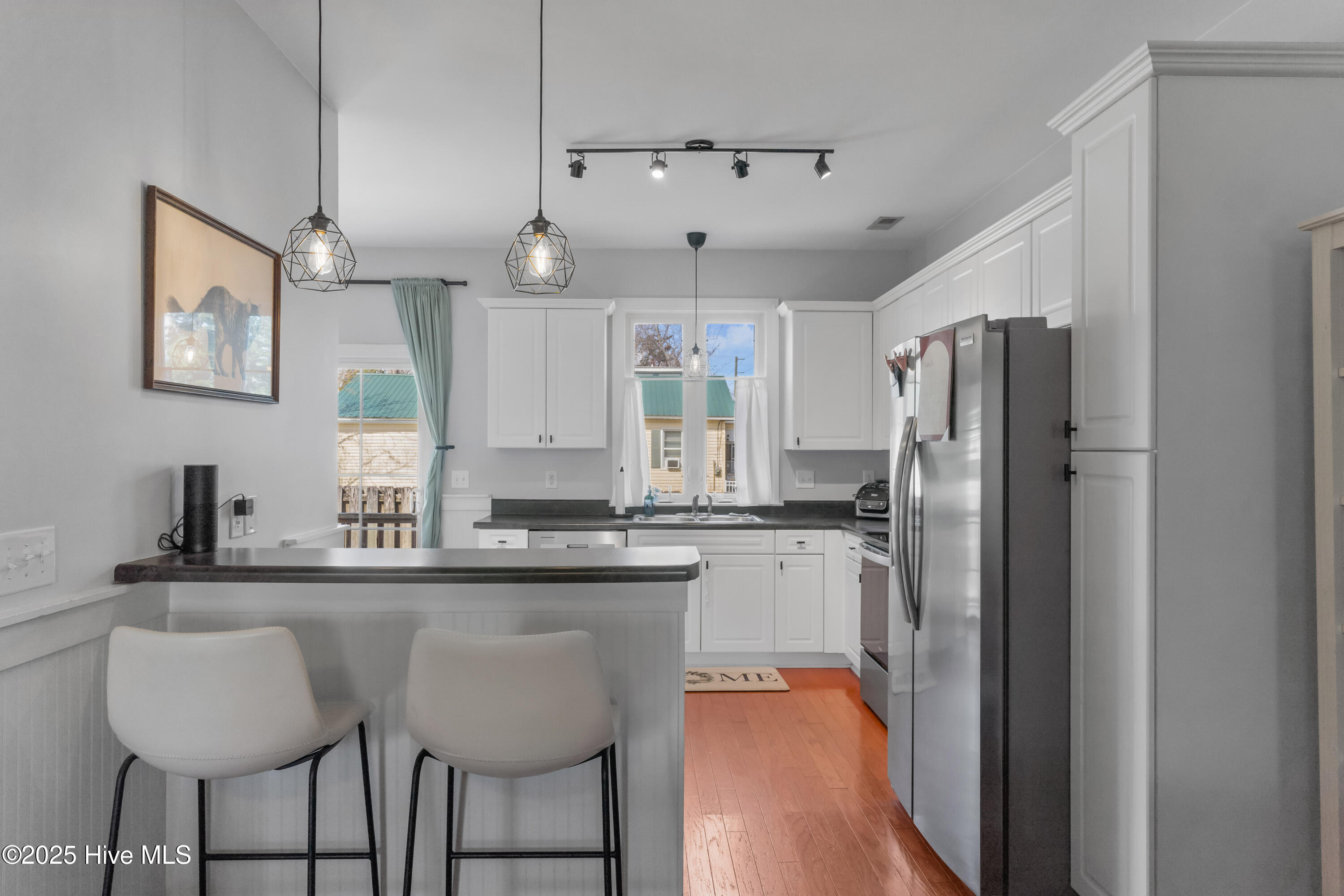 Kitchen with white cabinetry, a breakfast bar, stainless steel appliances, and warm wood floors.