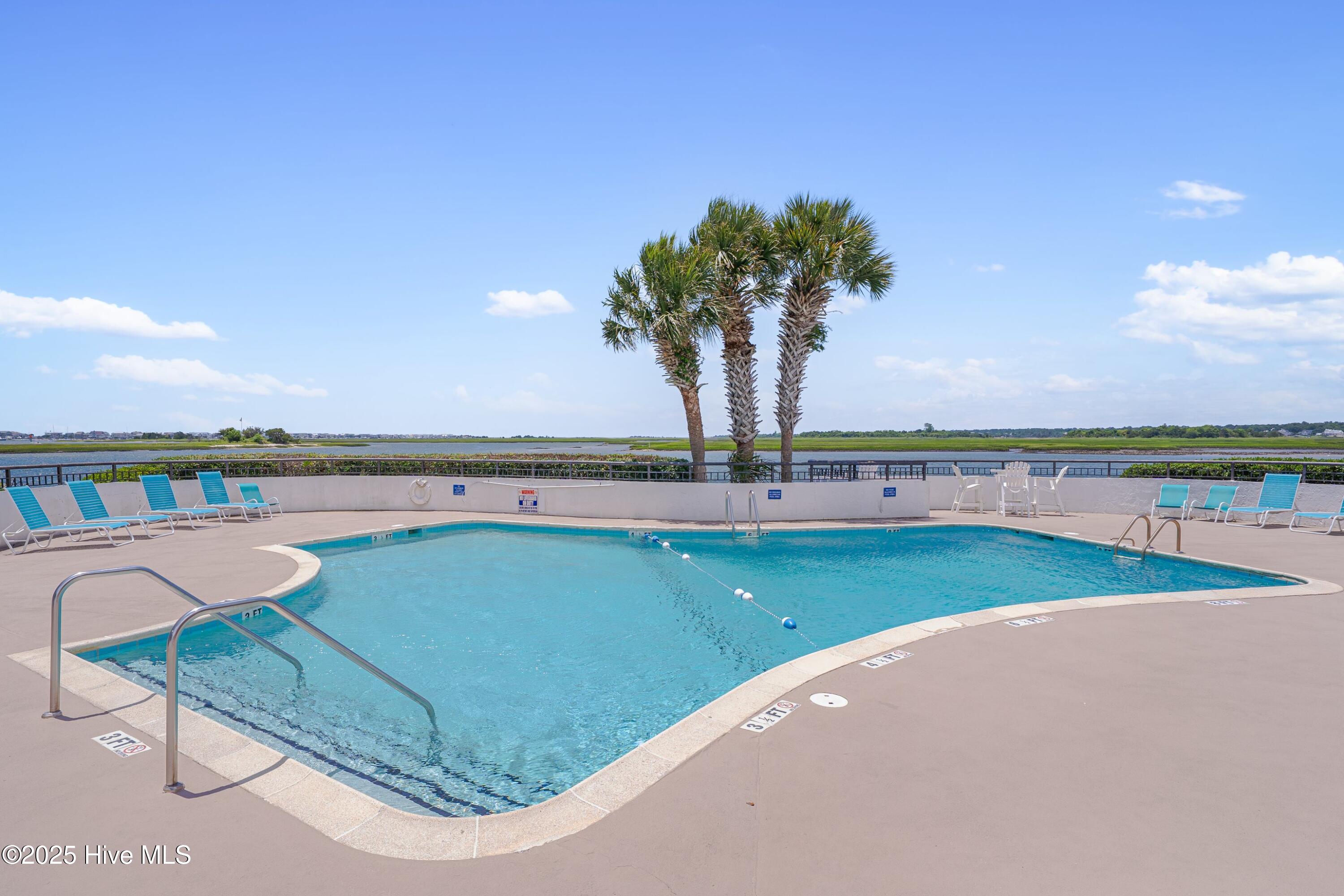 Outdoor pool with lounge chairs and palm trees overlooking a coastal marsh.