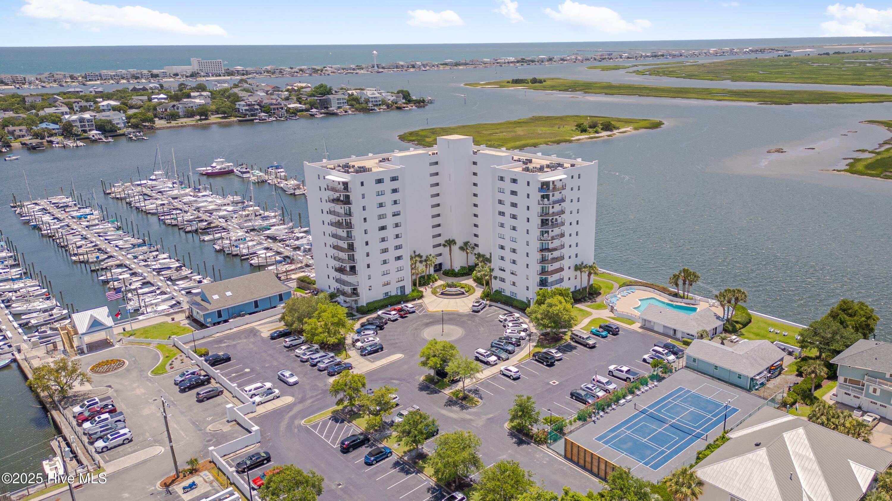 Waterfront condominium beside a marina, with a pool, tennis courts, and surrounding waterways.