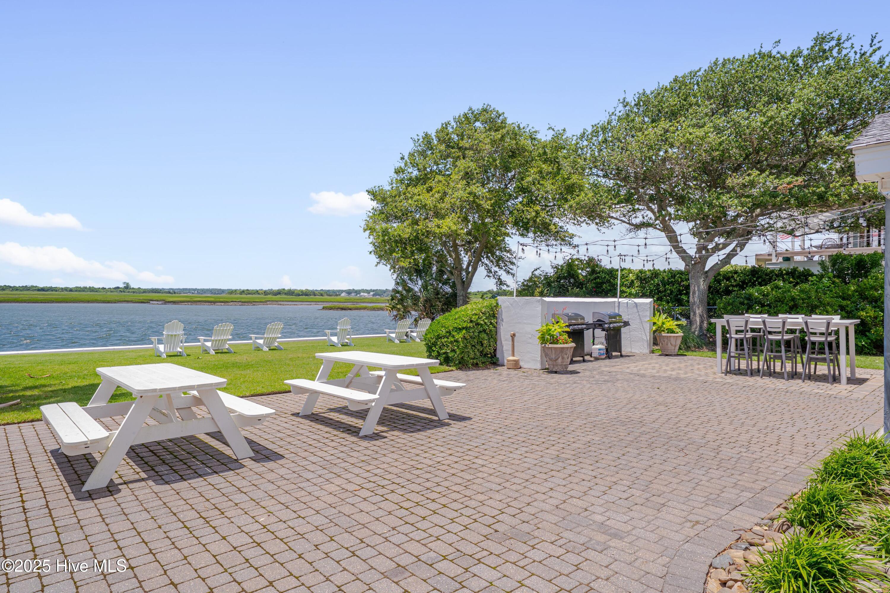 Waterfront patio with picnic tables, grills, and Adirondack chairs beside the water.