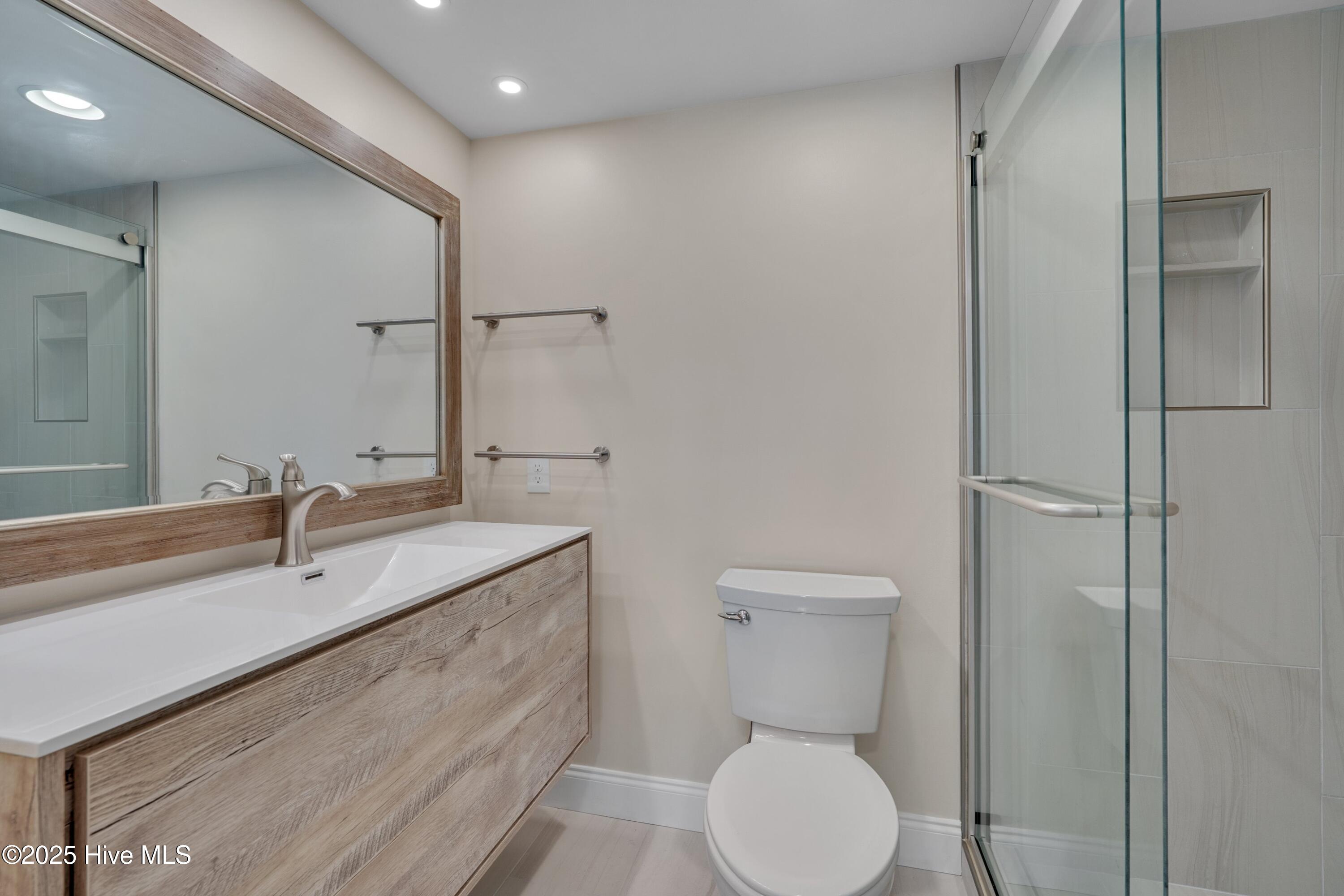 Bathroom with a wood-grain vanity, large framed mirror, and glass-enclosed shower.