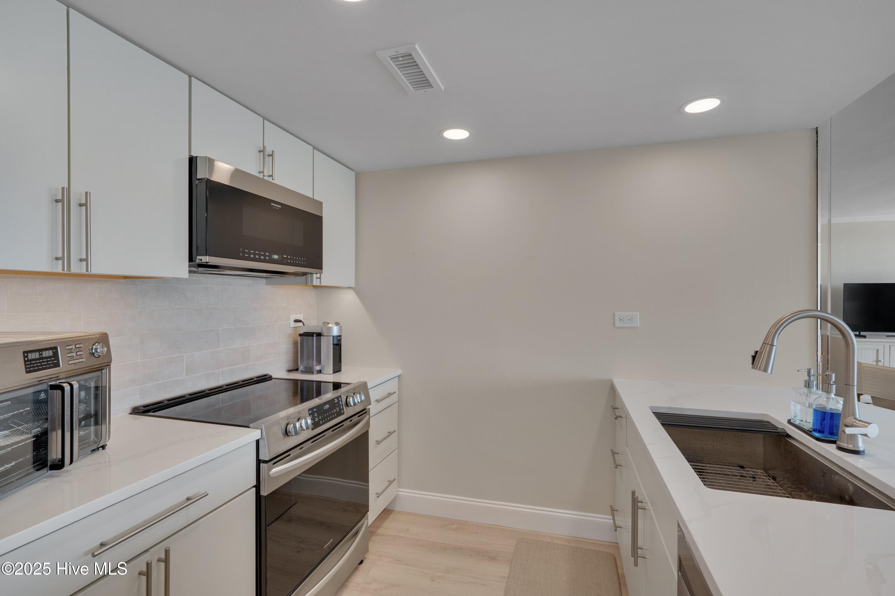 Modern kitchen with white cabinets, stainless-steel appliances, and a deep sink with a tall faucet.