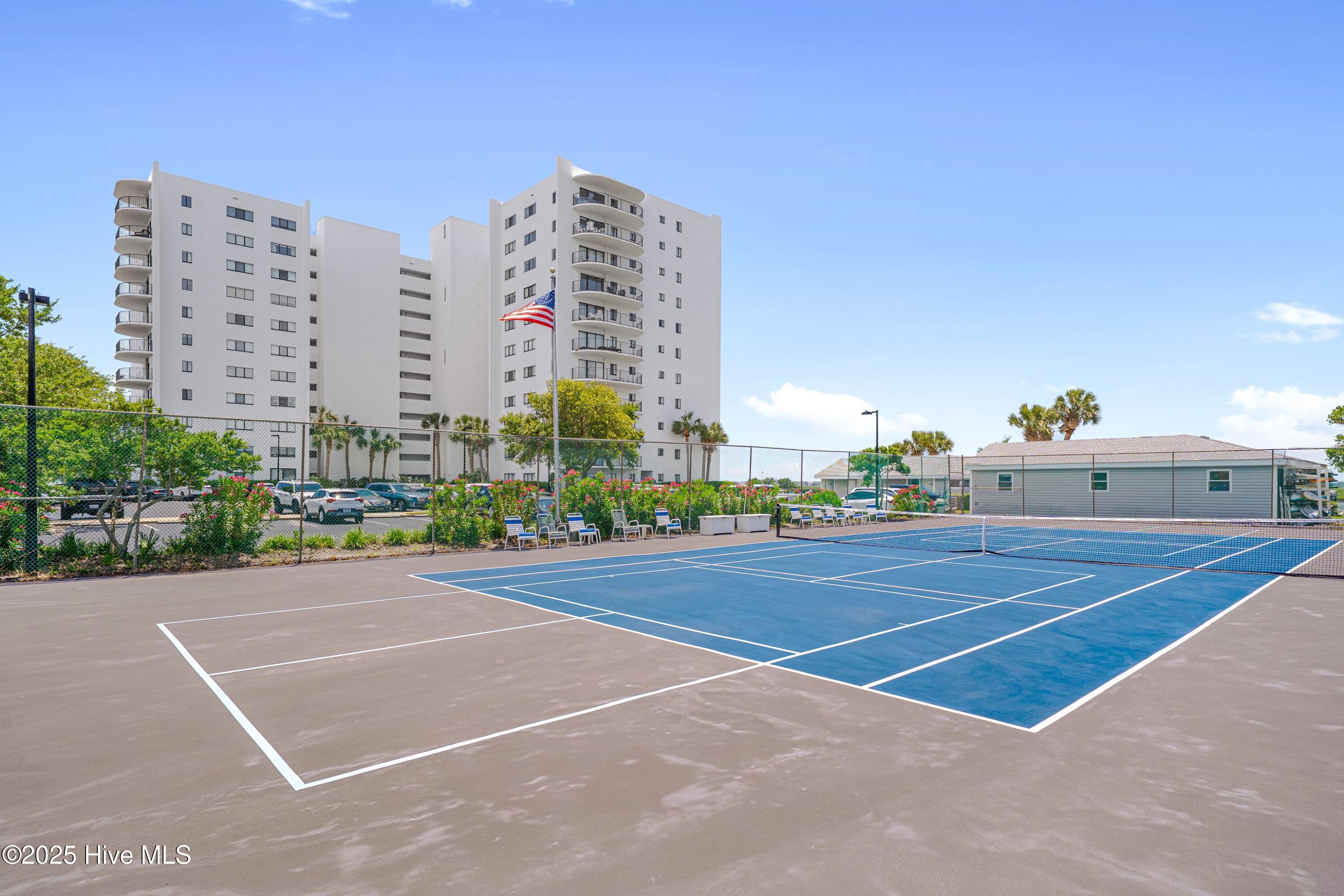 Outdoor tennis courts in front of a white condominium building with curved balconies.