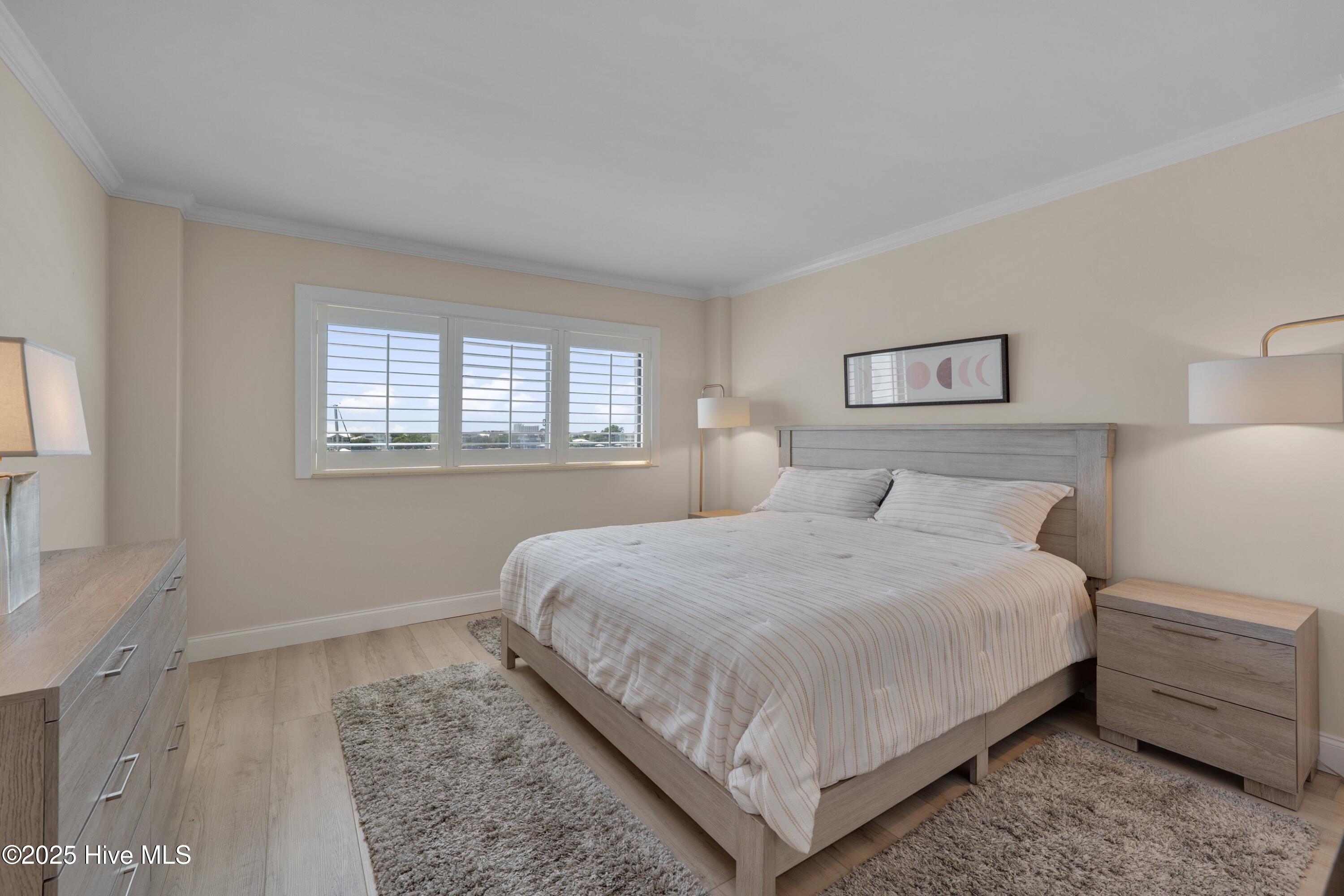Furnished bedroom with a gray wood bed and shuttered windows overlooking a coastal view.