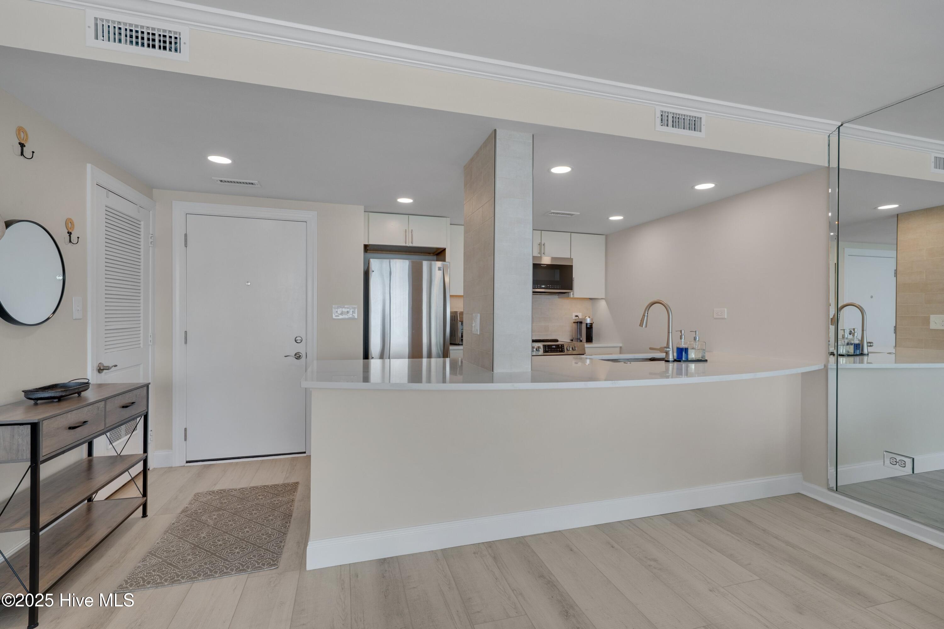 Condo kitchen with a curved white peninsula, stainless steel refrigerator, and full-height mirrored wall.