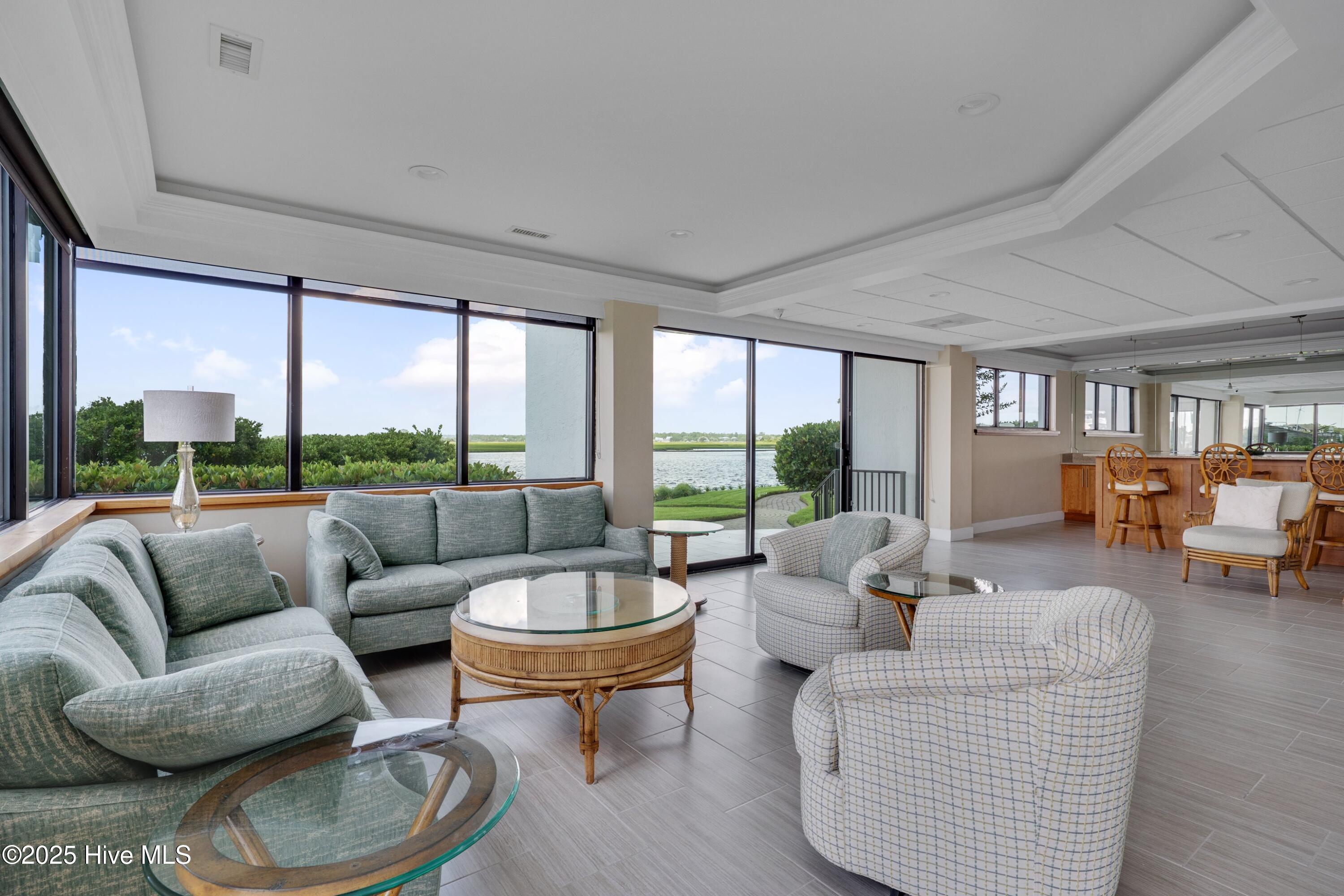 Furnished living room with expansive windows overlooking the water and landscaped grounds.