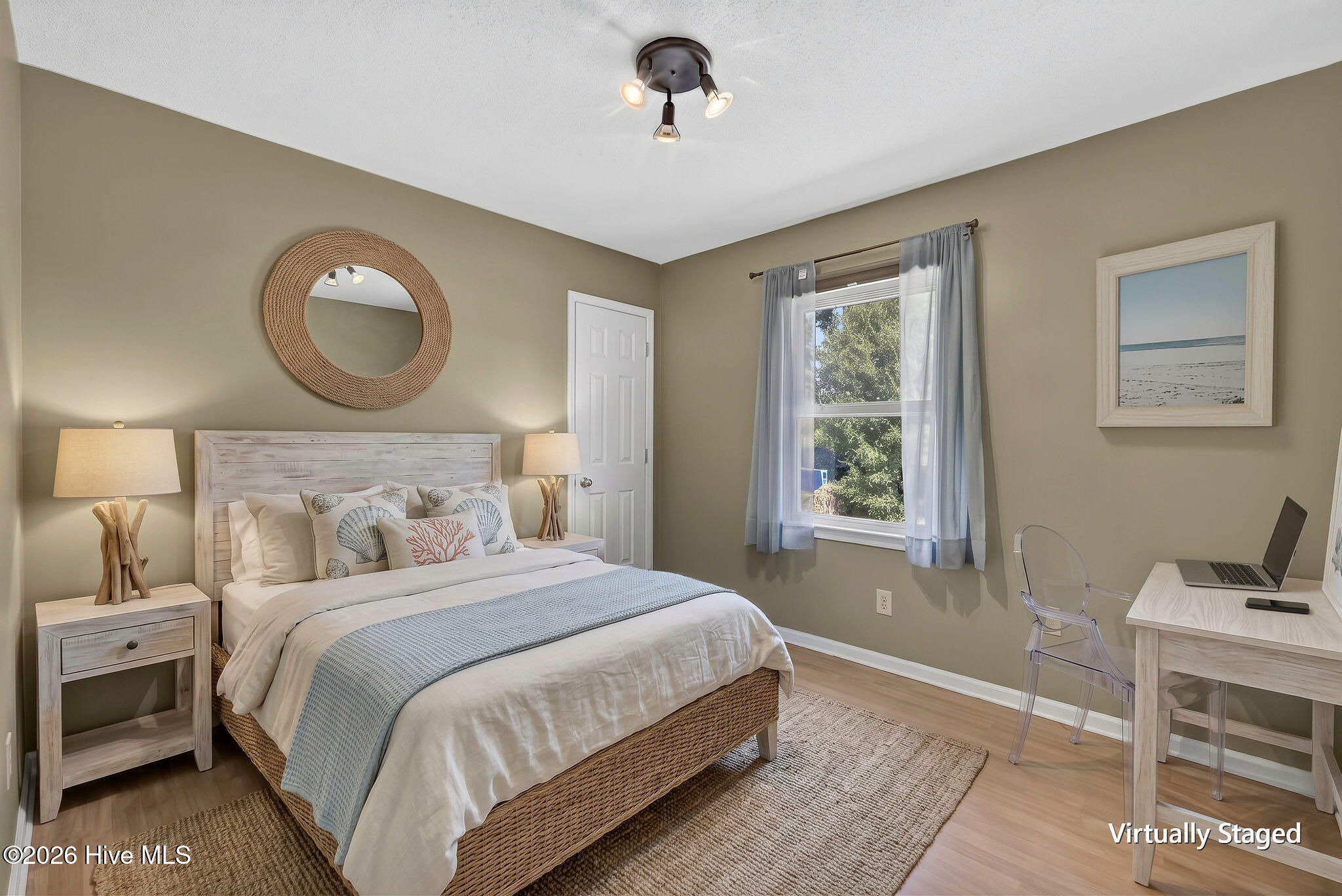 Virtually staged bedroom with a woven bed, blue throw, window, and desk.