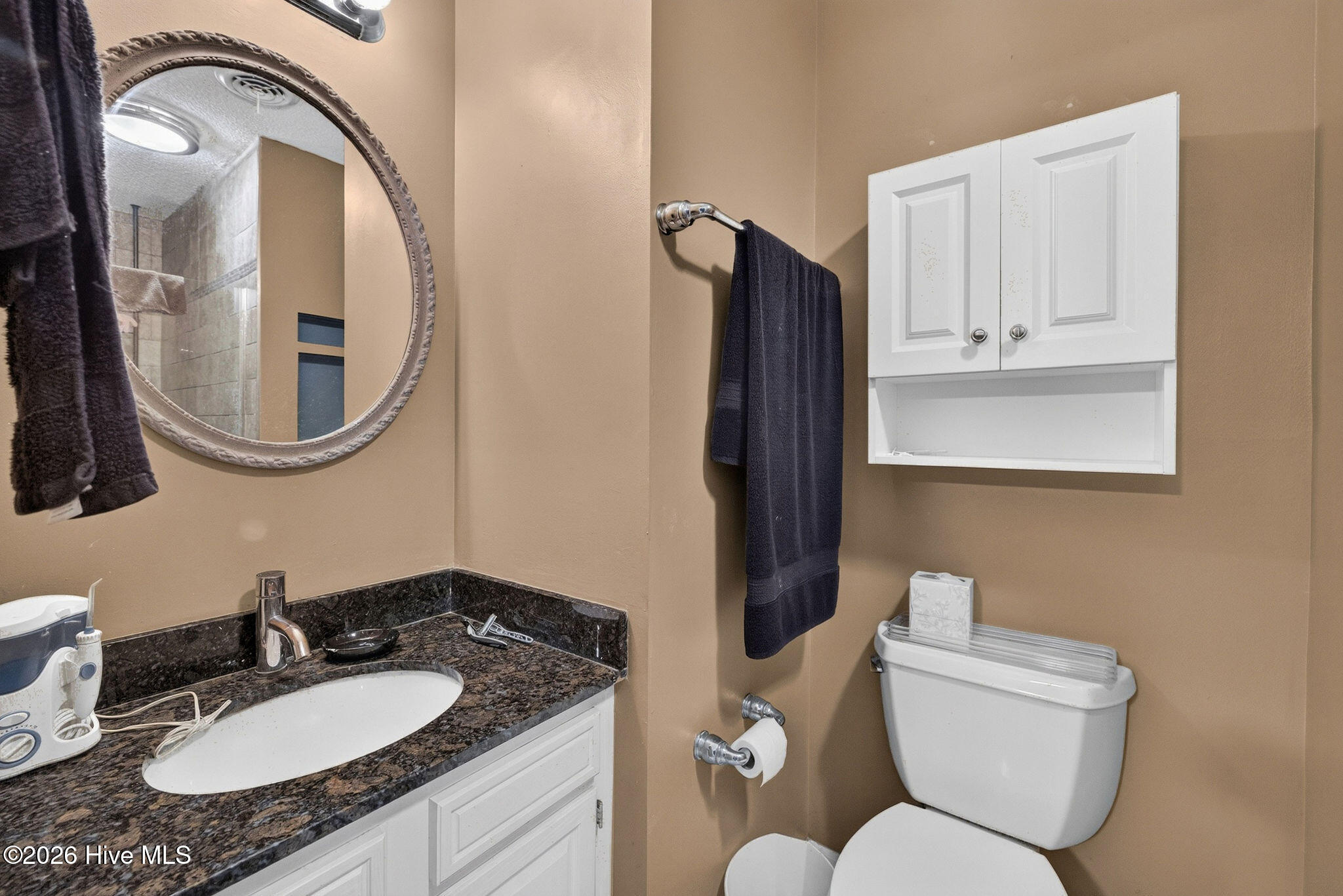 Bathroom with a dark granite vanity, round mirror, white wall cabinet, and toilet.