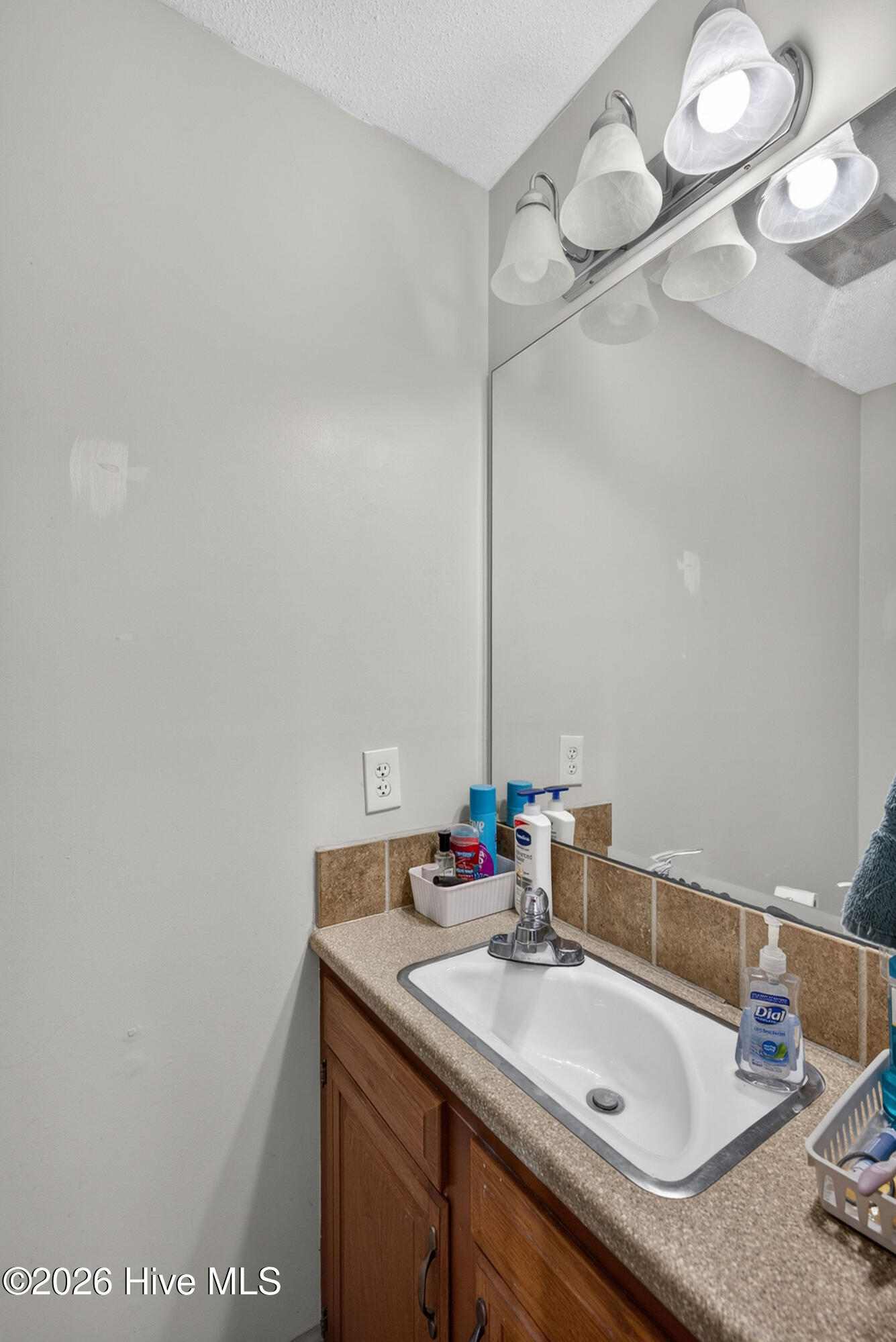 Bathroom vanity with a white sink, tan tile backsplash, wood cabinets, and mirror.