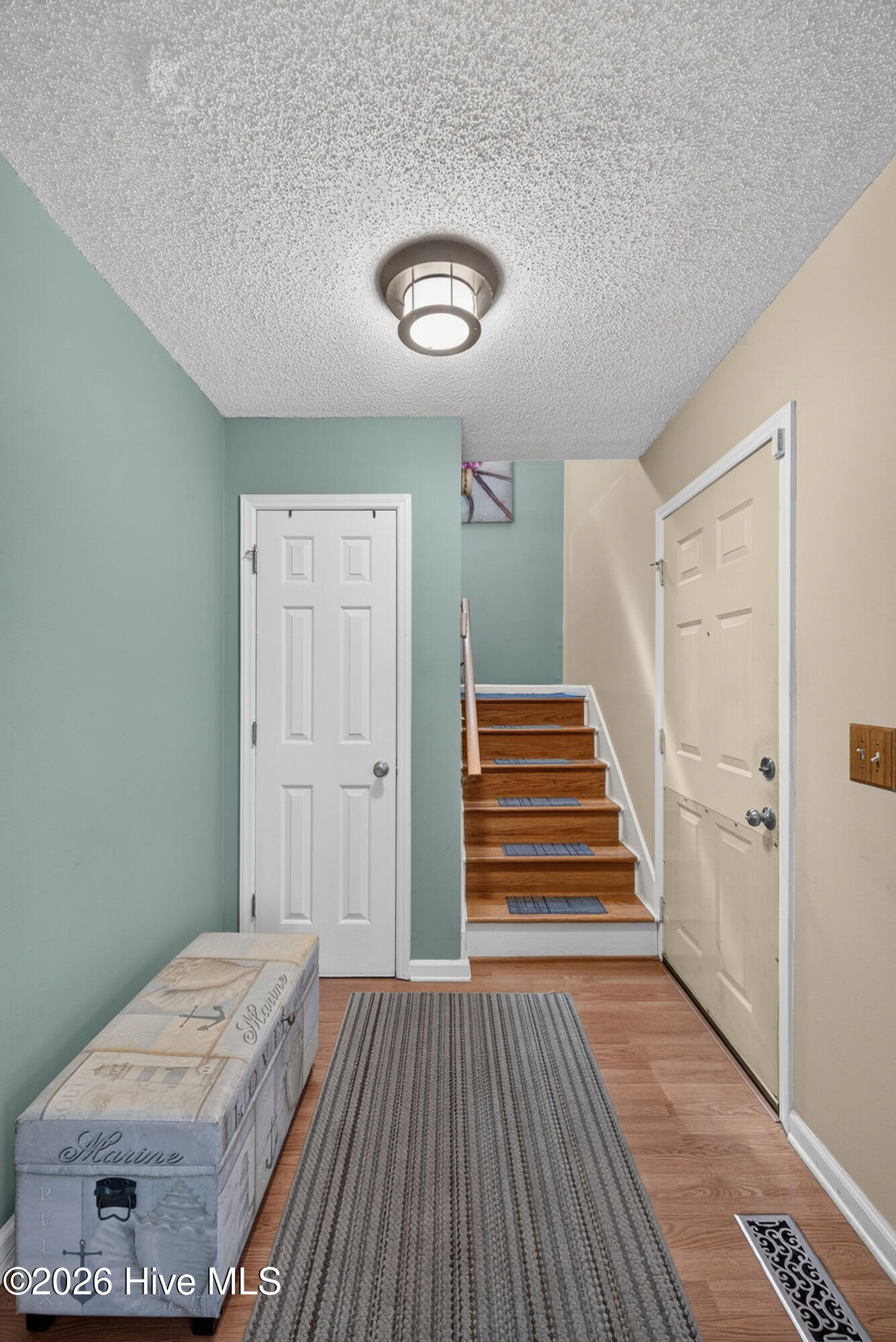 Entry hall with a gray runner, vintage trunk, and short wooden staircase.