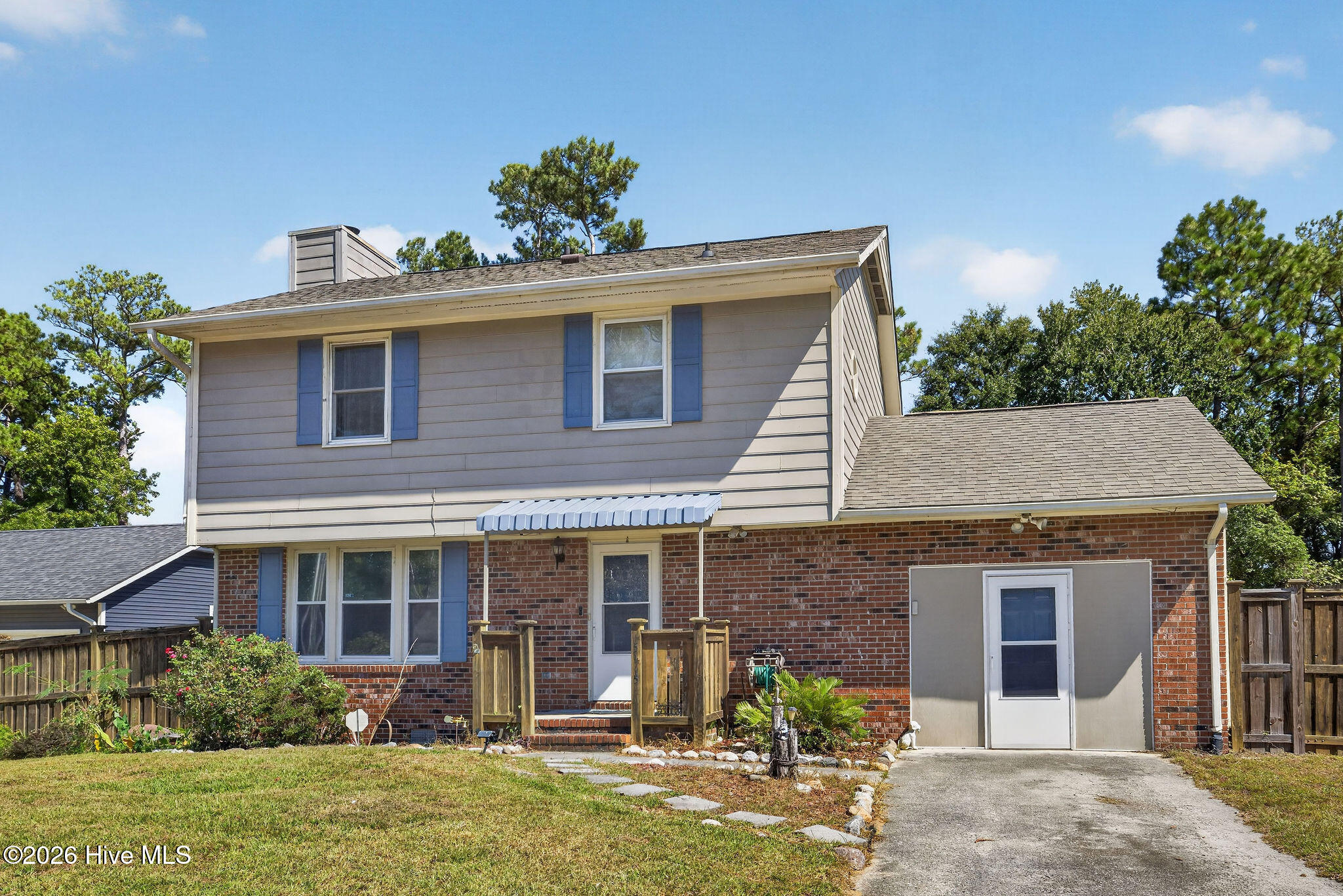 Rear exterior of a two-story brick and siding house with blue shutters, small deck, and driveway.
