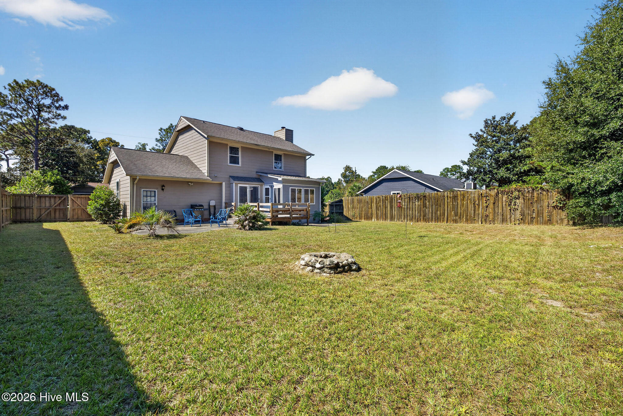 Two-story house behind a spacious fenced backyard with patio seating and a stone fire pit.