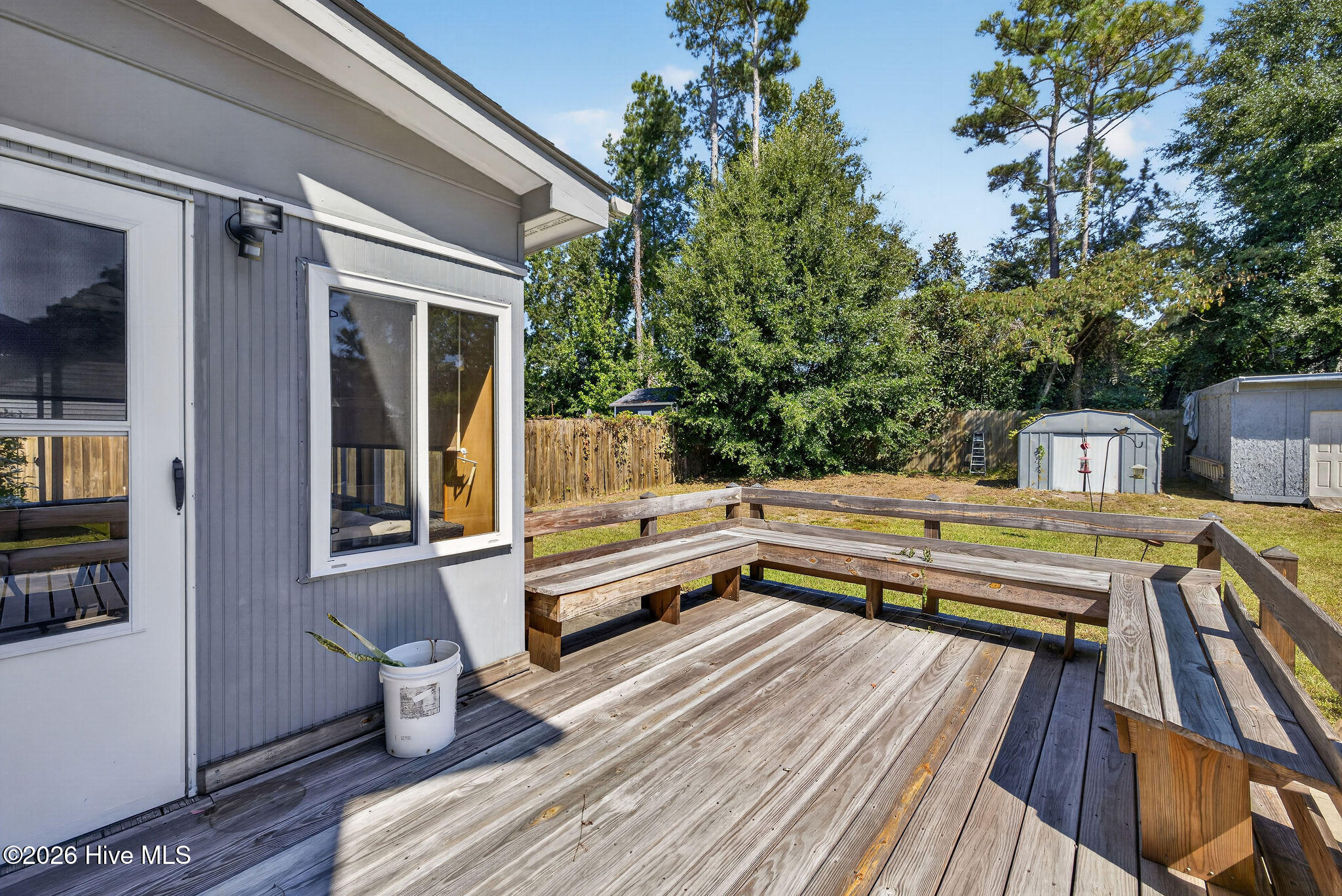 Backyard deck with built-in wooden benches overlooking a fenced, tree-lined yard.