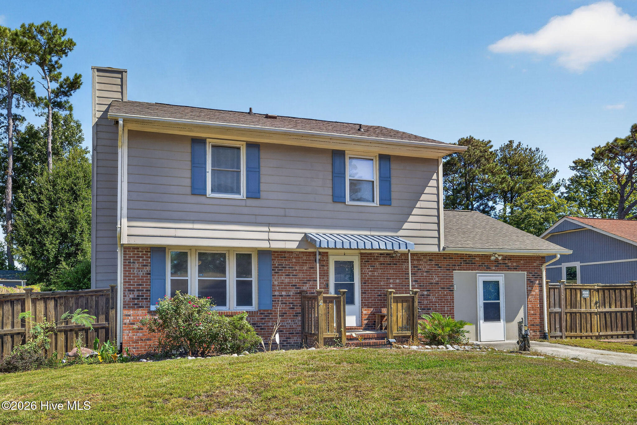 Two-story home's rear exterior with brick and gray siding, blue shutters, and a striped awning.