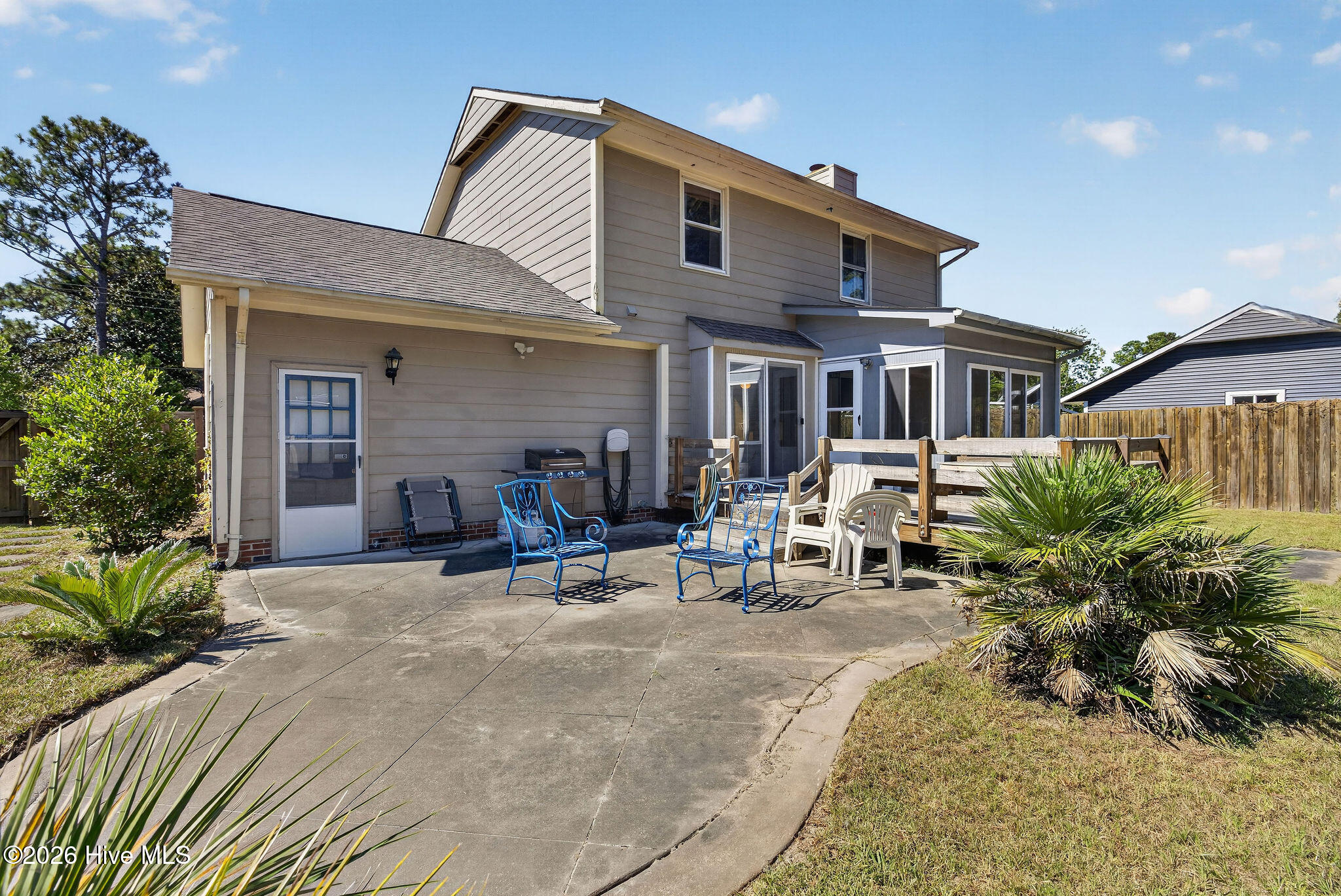 Two-story house with a concrete patio, raised deck, outdoor seating, and fenced yard.