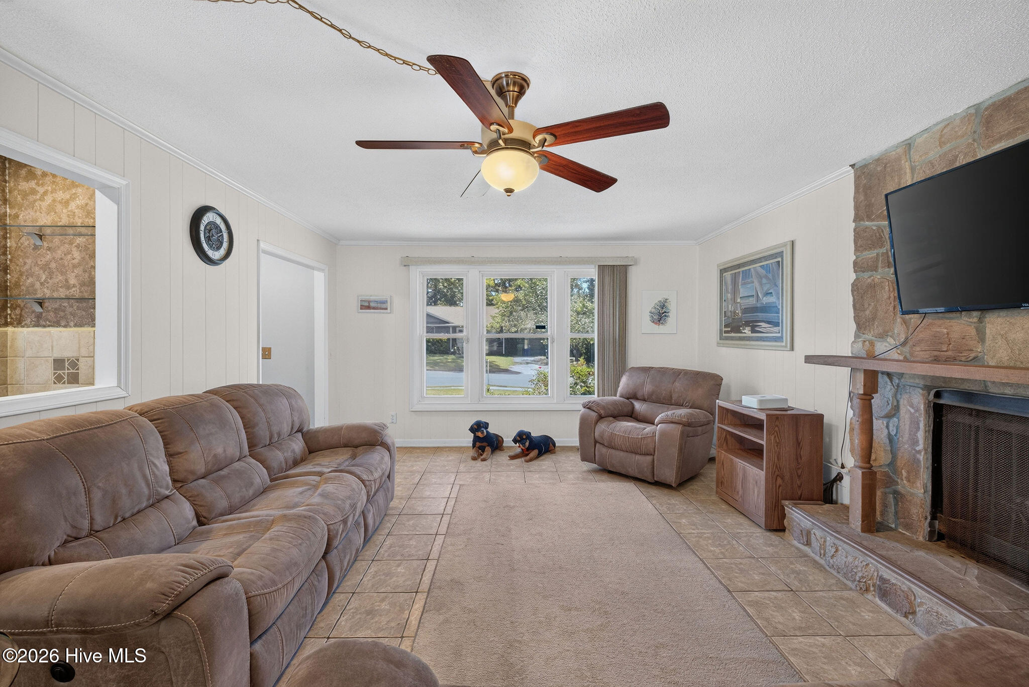 Living room with brown leather seating, a stone fireplace, and two small dog figures by the windows.