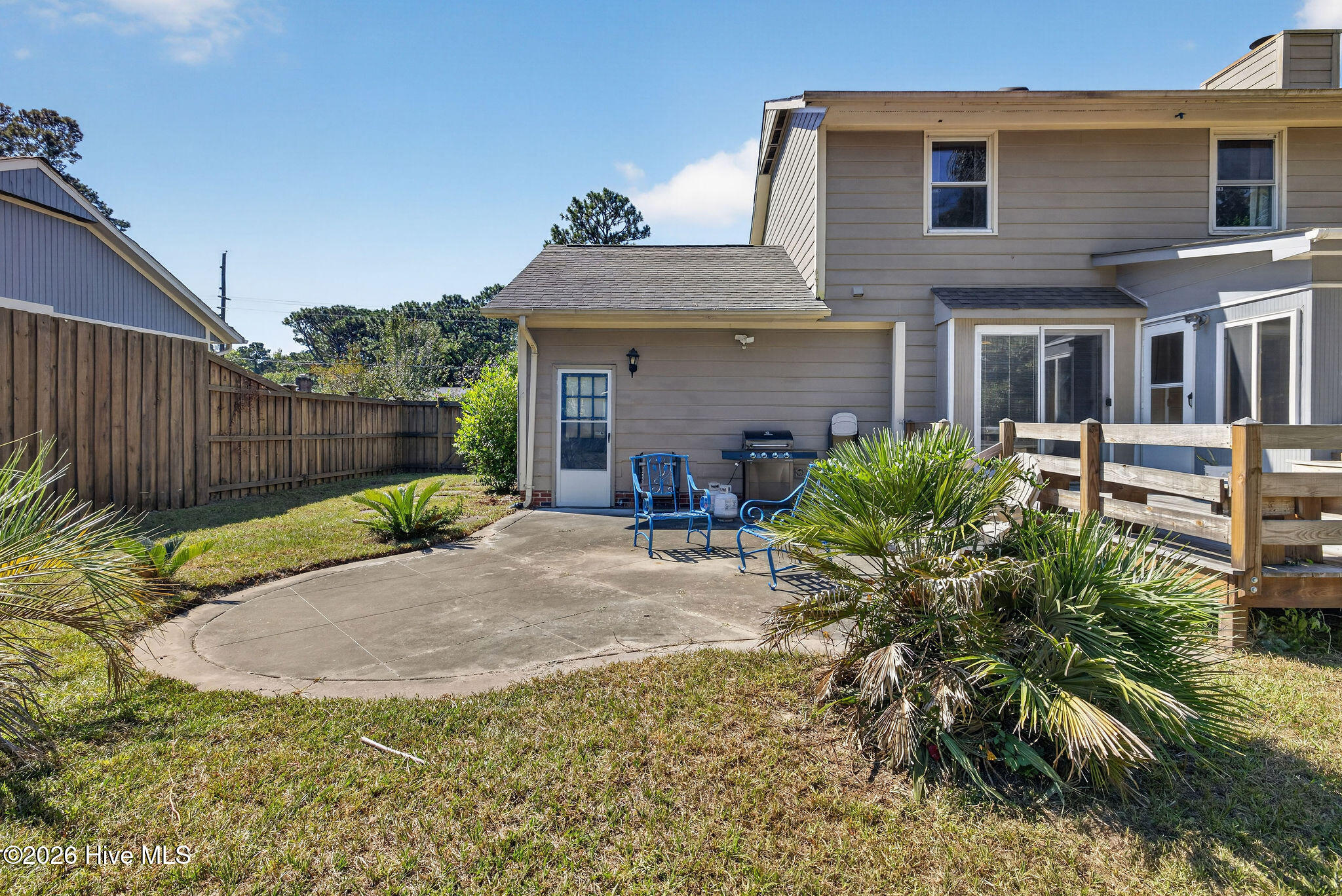 Backyard patio with blue chairs and a grill beside the fenced yard.