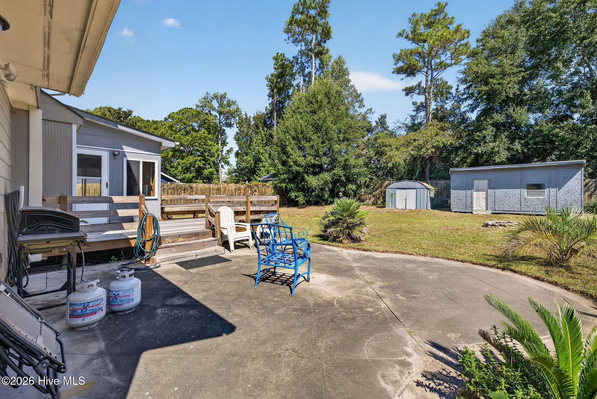 Backyard patio and deck with outdoor seating, a grill, lawn, and two storage sheds.