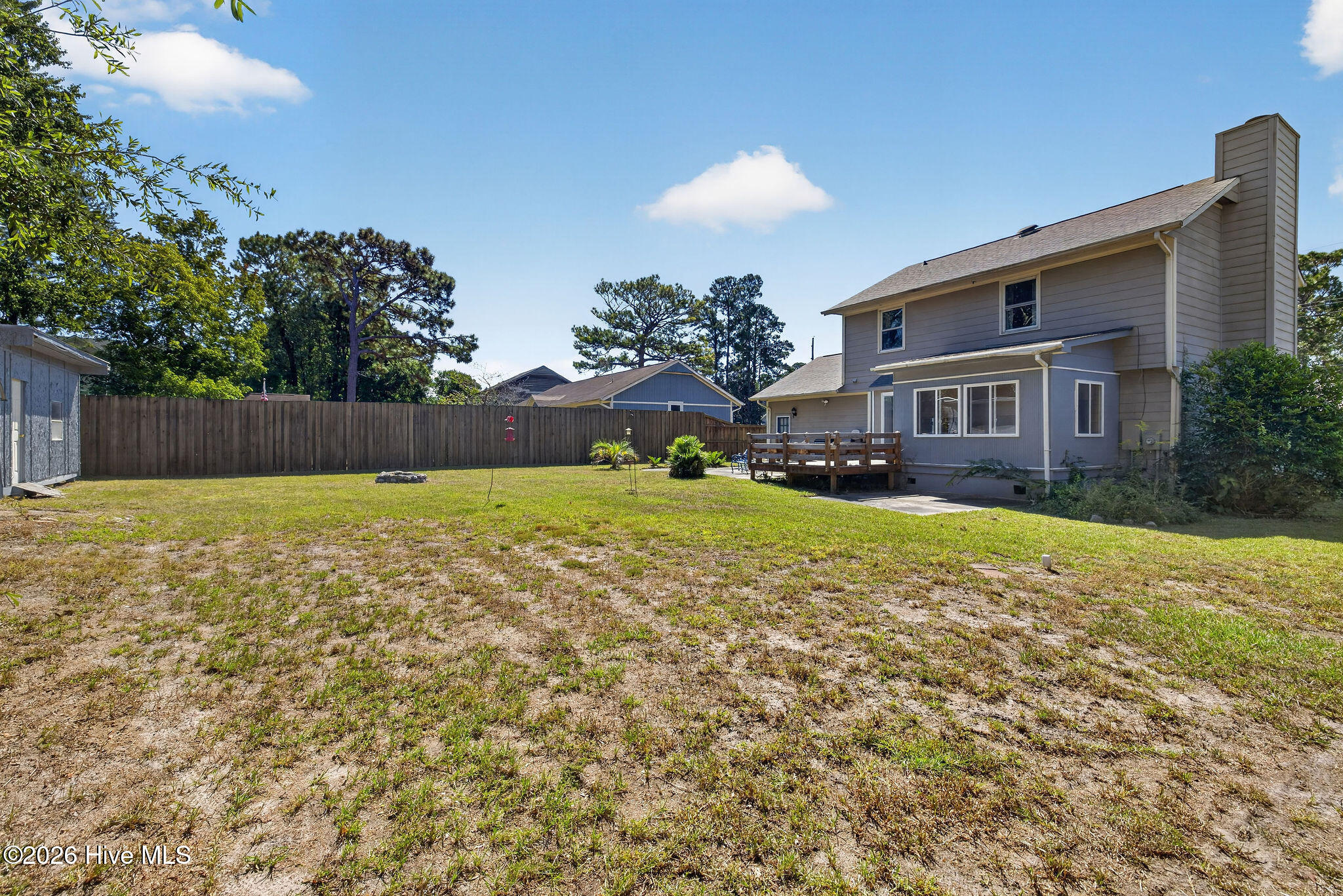 Rear of a two-story gray house with a wooden deck and broad fenced backyard.