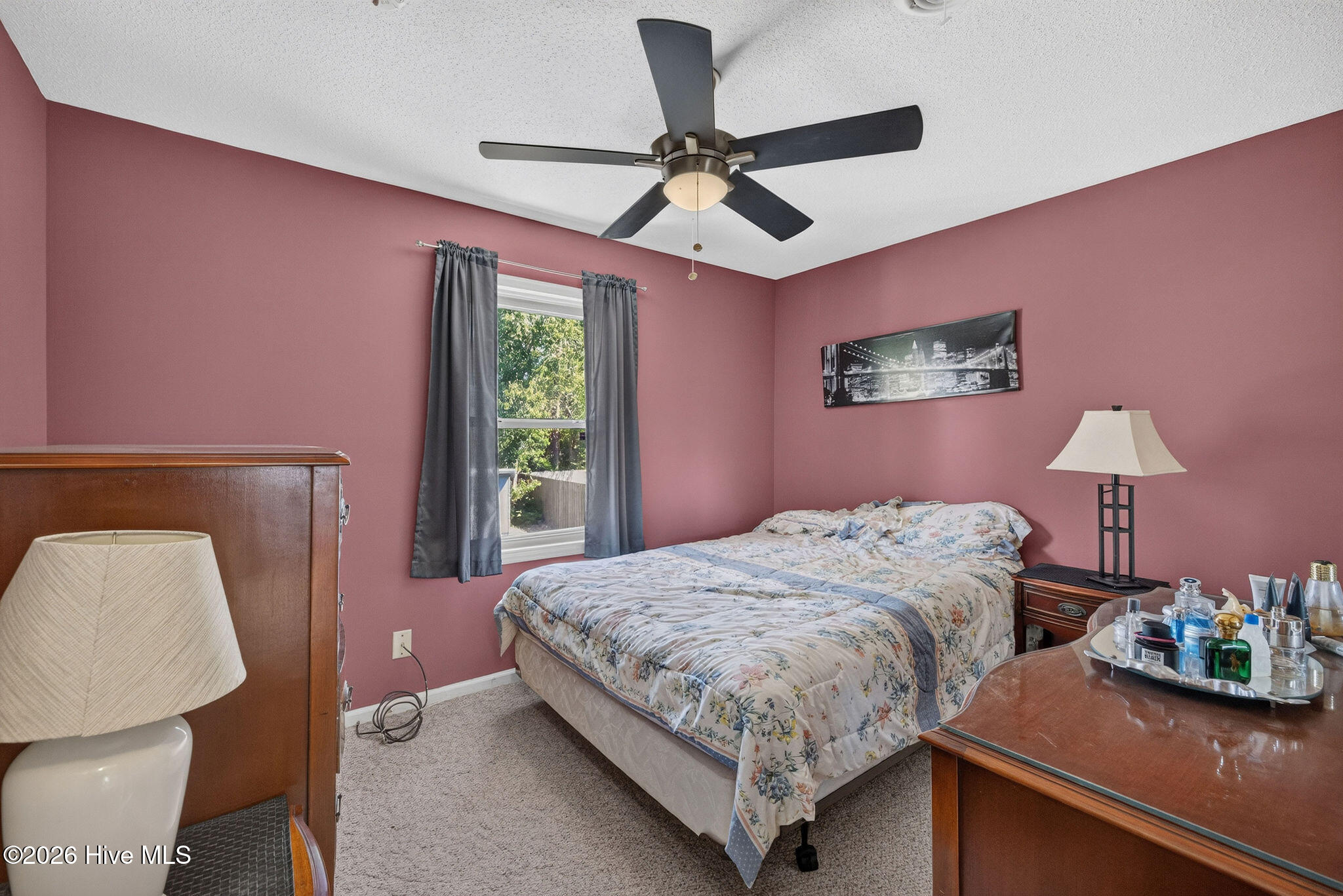 Bedroom with pink walls, floral bedding, gray curtains, and a dark ceiling fan.