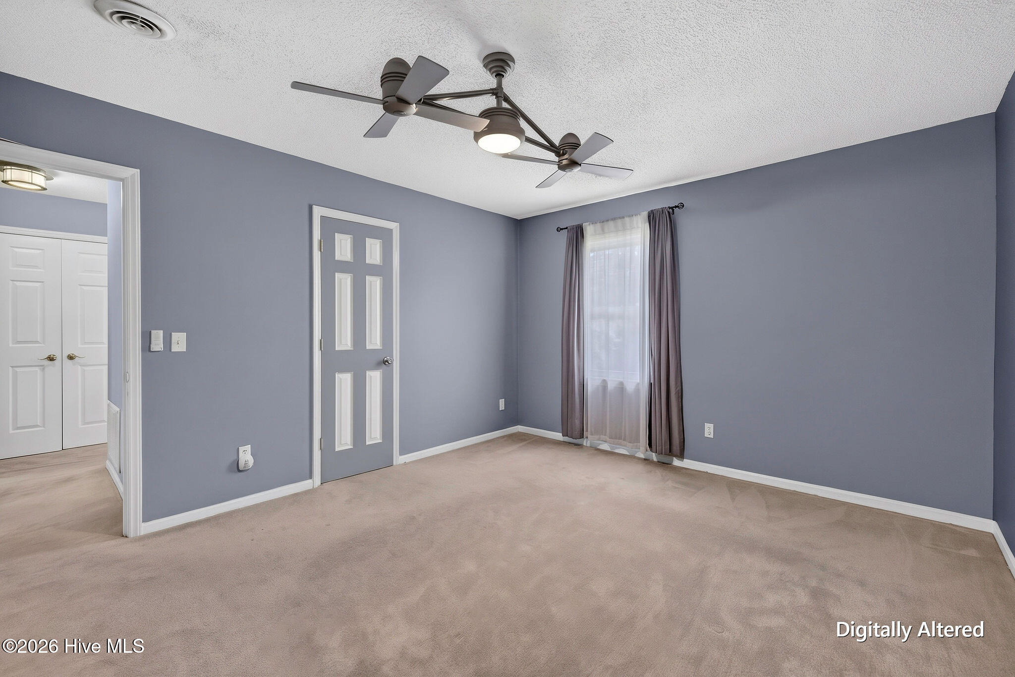 Empty bedroom with gray walls, beige carpet, a curtained window, and a two-fan ceiling fixture.