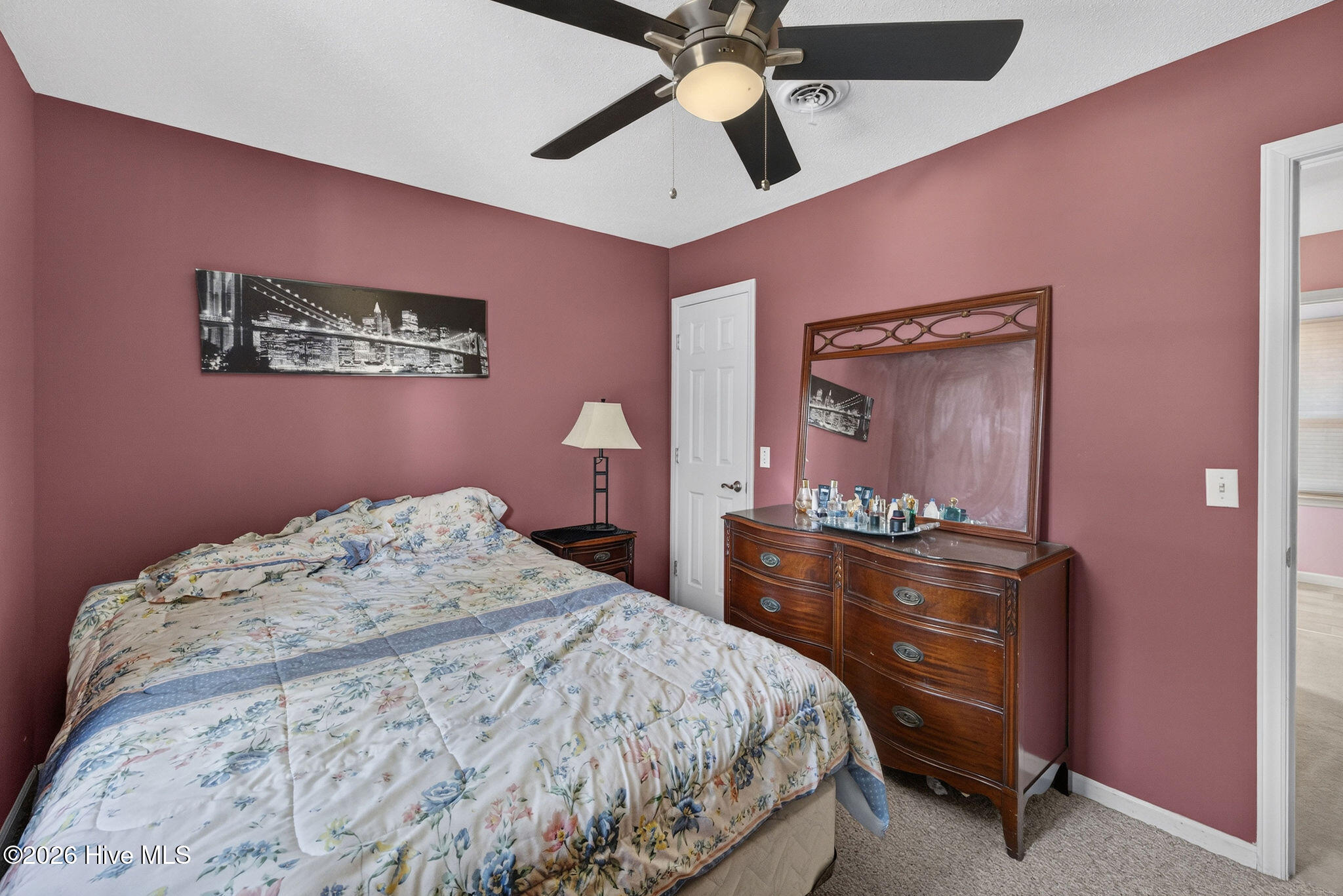 Bedroom with mauve walls, a floral quilted bed, ceiling fan, and wooden dresser with mirror.