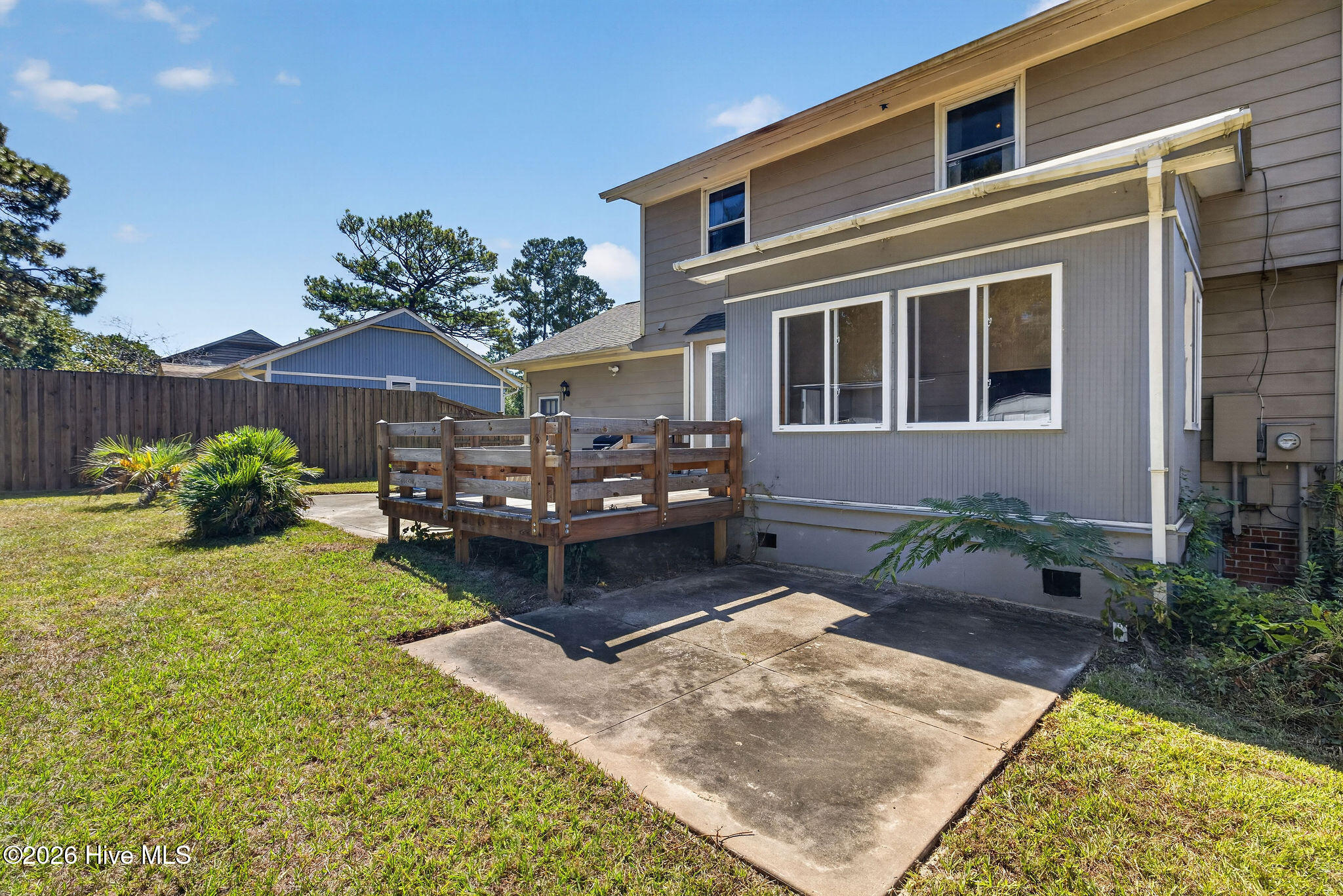 Rear of a two-story house with a raised wooden deck and concrete patio.