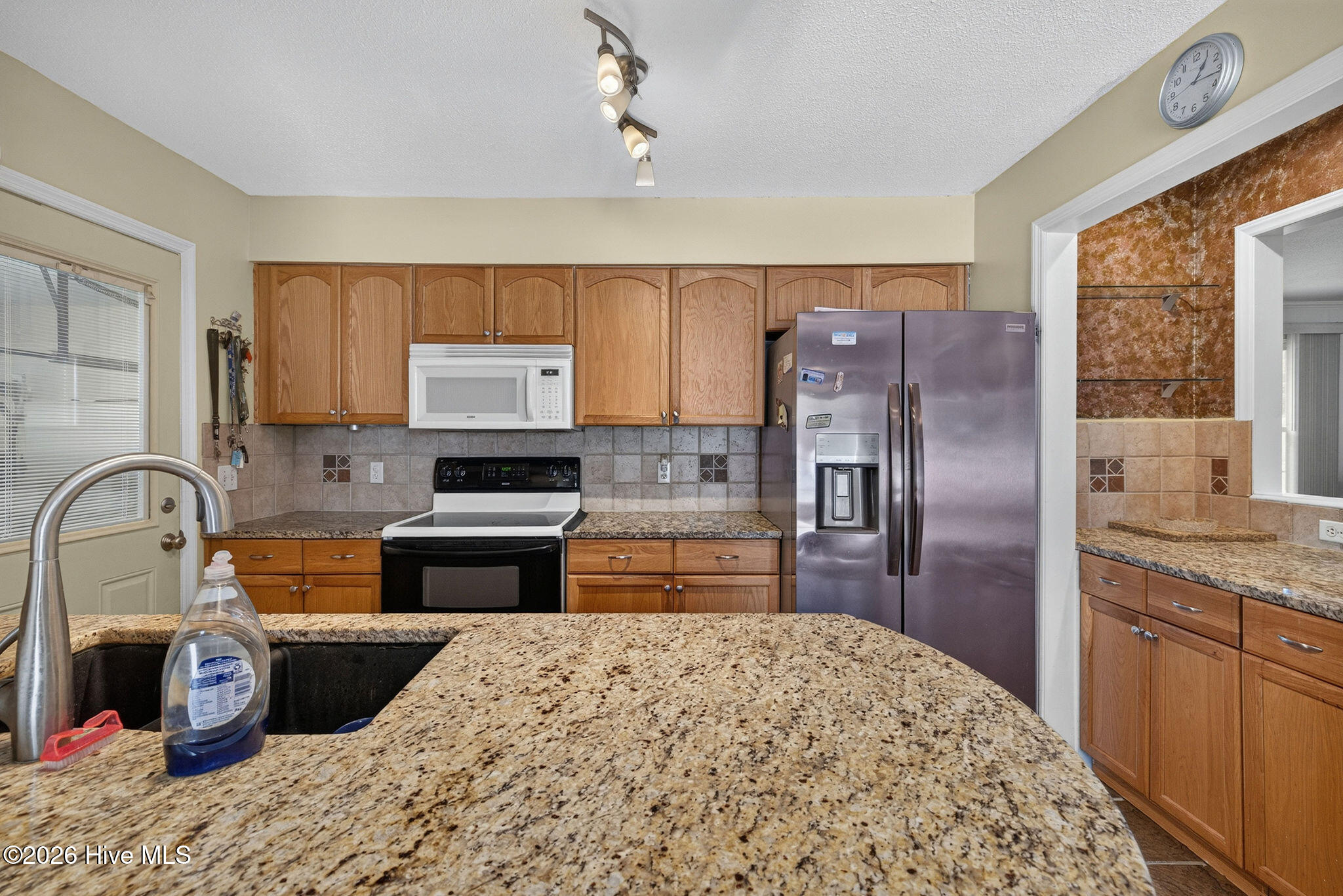 Kitchen with granite countertops, wood cabinetry, stainless refrigerator, and black range.
