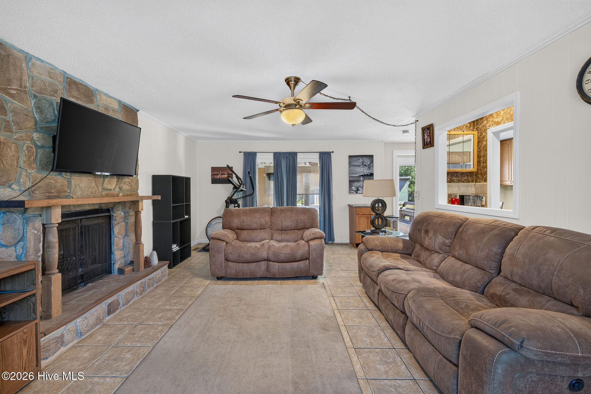 Living room with a stone fireplace, mounted television, and brown reclining sofas.