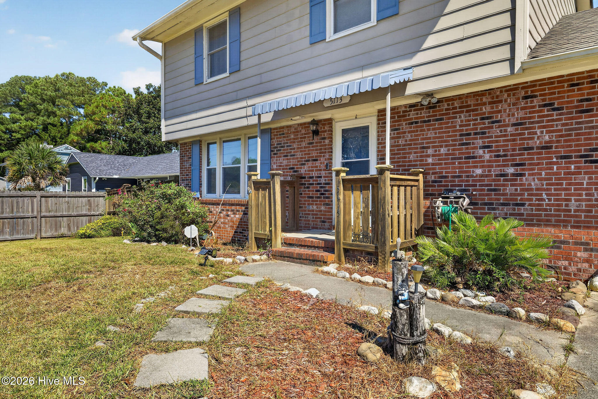 Two-story home with a brick facade, blue shutters, wooden front porch, and stepping-stone garden path.