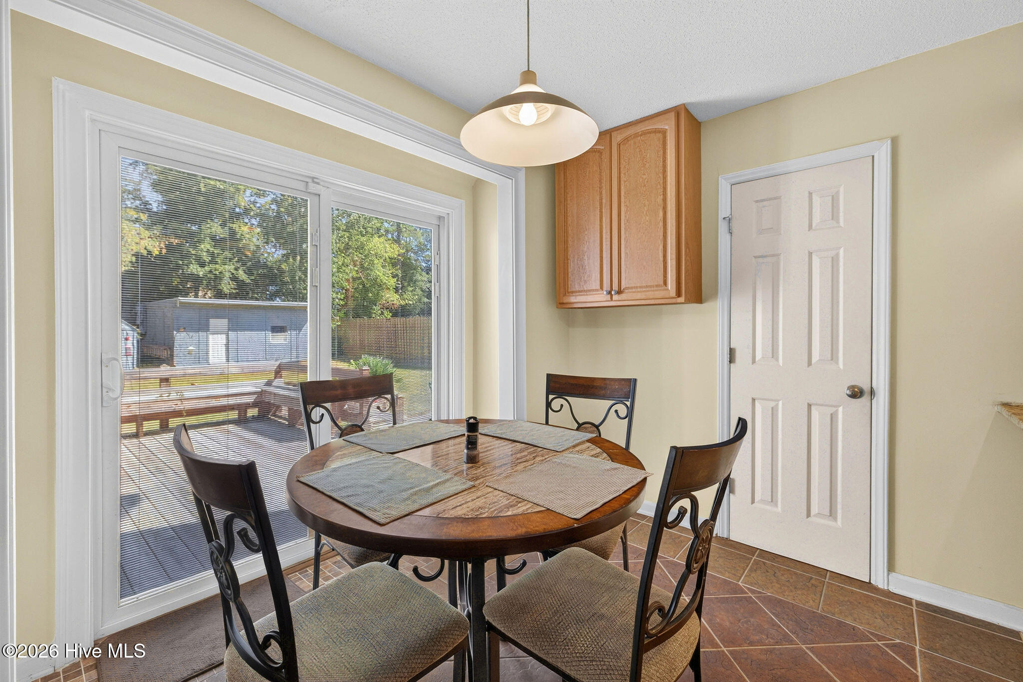 Dining area with a round wooden table beside sliding glass doors opening onto a deck.