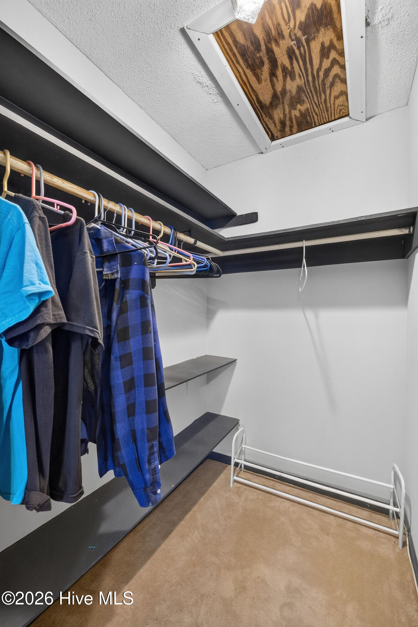 Walk-in closet with hanging clothes, dark shelving, a shoe rack, and a ceiling access hatch.
