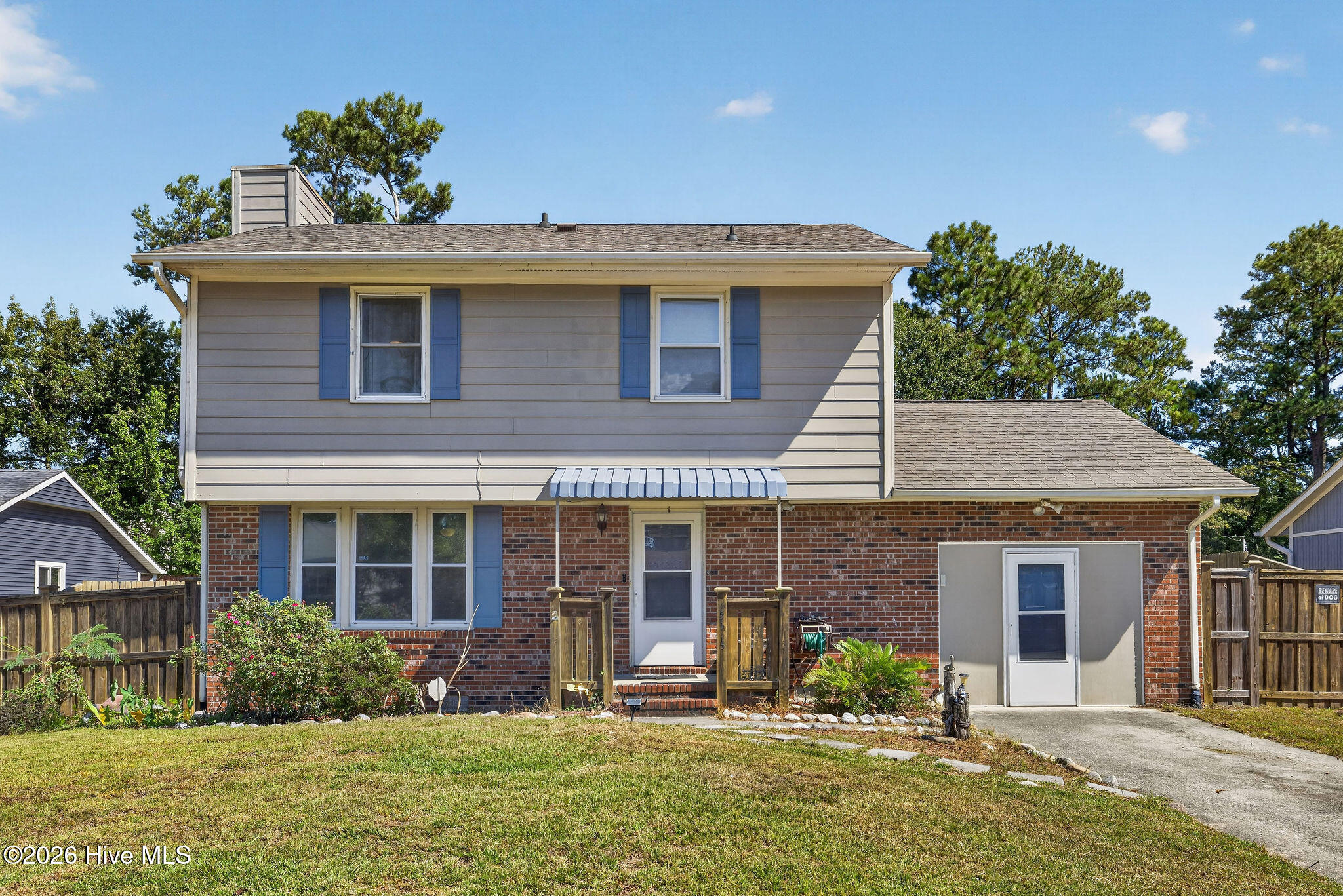 Two-story home’s rear exterior with brick lower level, blue shutters, back door awning, and driveway.