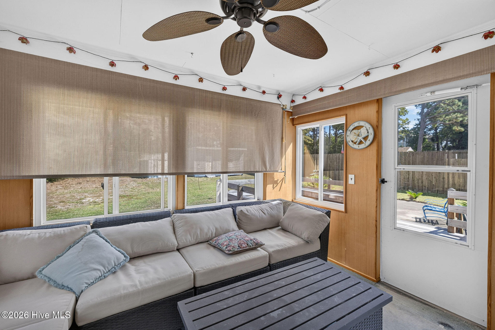 Enclosed sunroom with a sectional sofa, wood-paneled walls, wide windows, and a glass door to the patio.