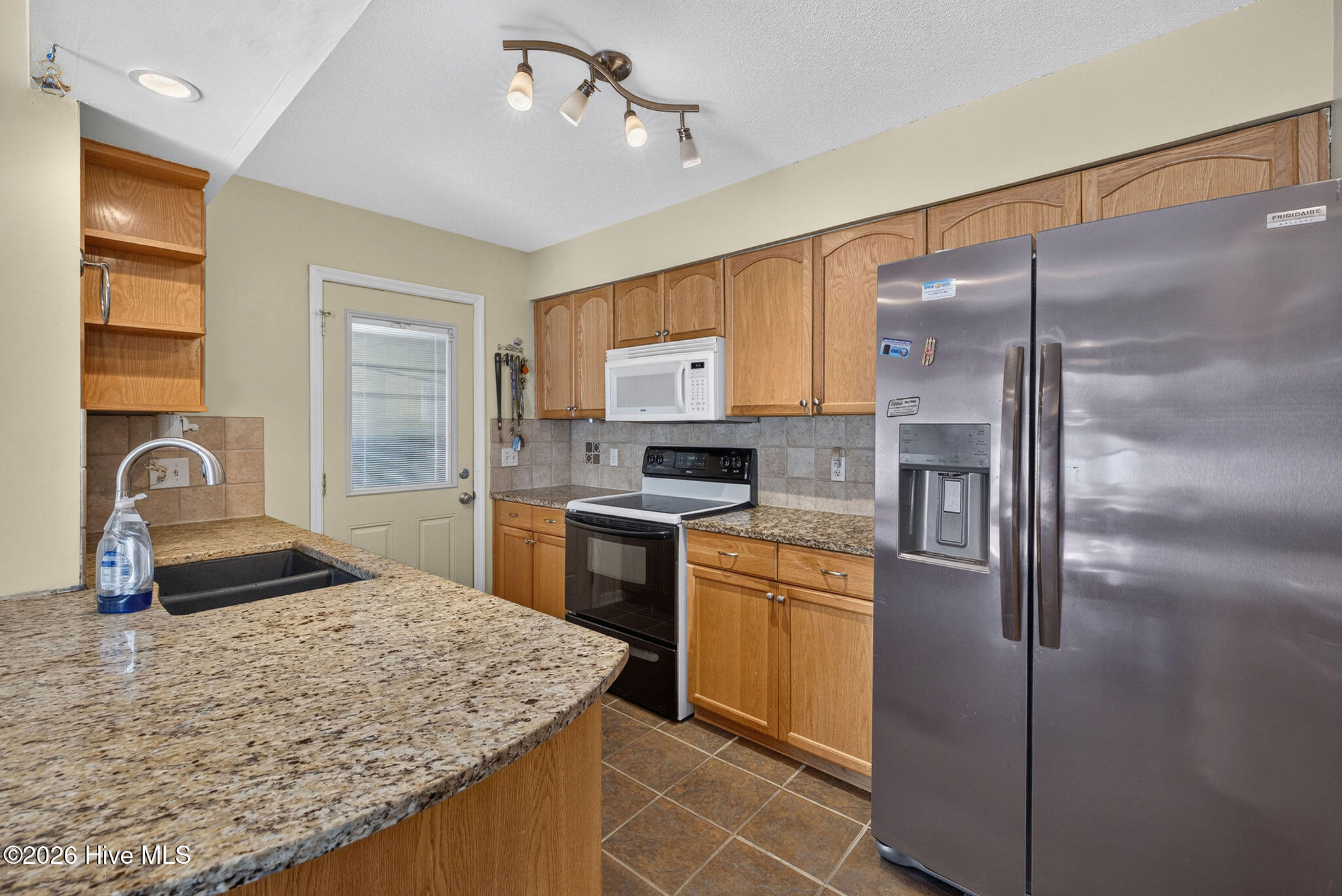 Kitchen with wood cabinetry, granite peninsula, stainless refrigerator, and range with microwave.