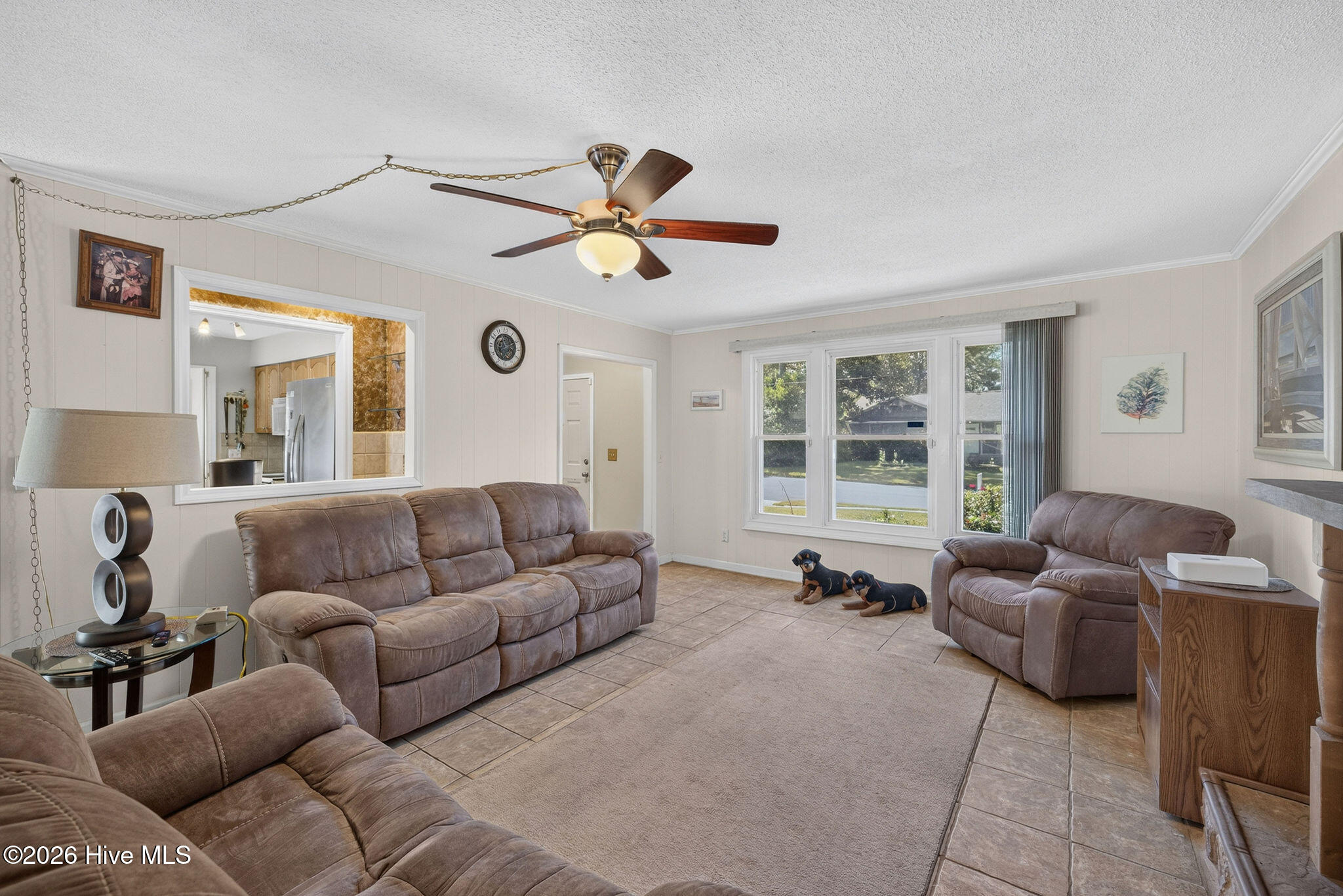 Living room with brown reclining sofas, tiled floors, and a large window overlooking the yard.