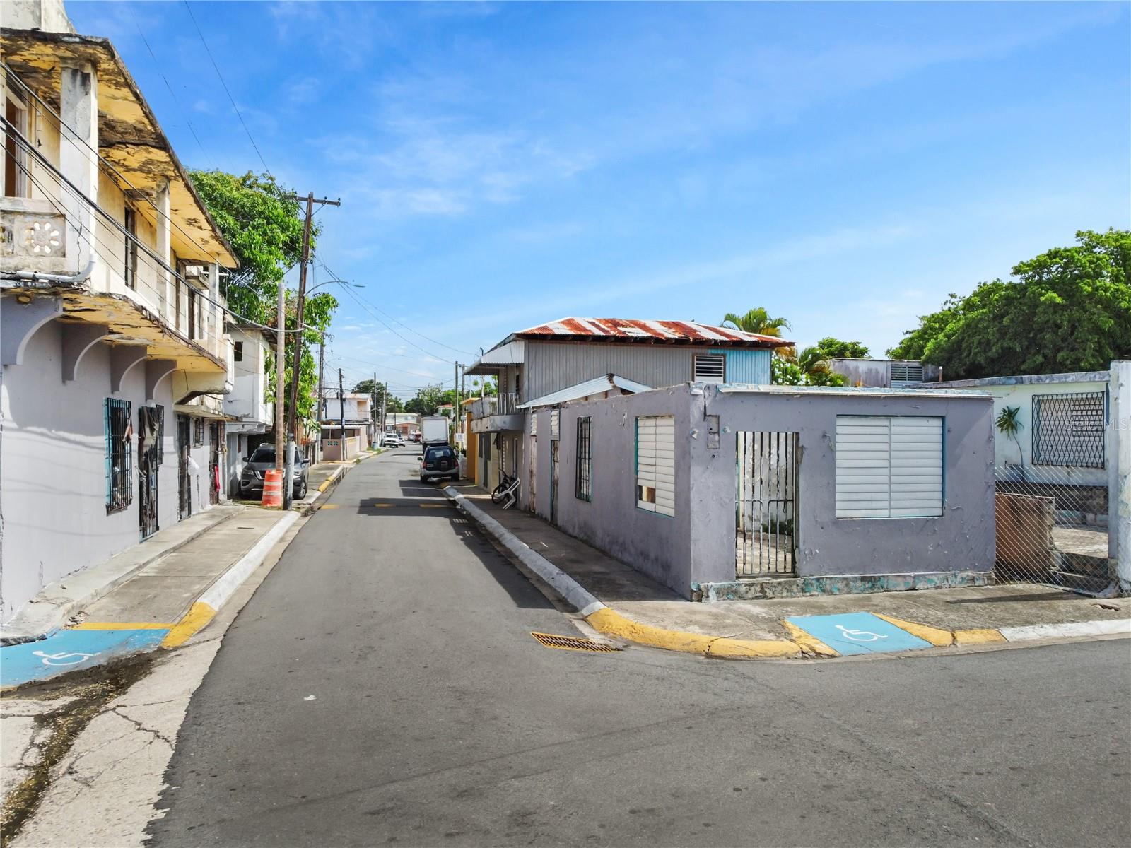 Street in Cataño lined with low-rise buildings, parked cars, and accessible parking spaces.