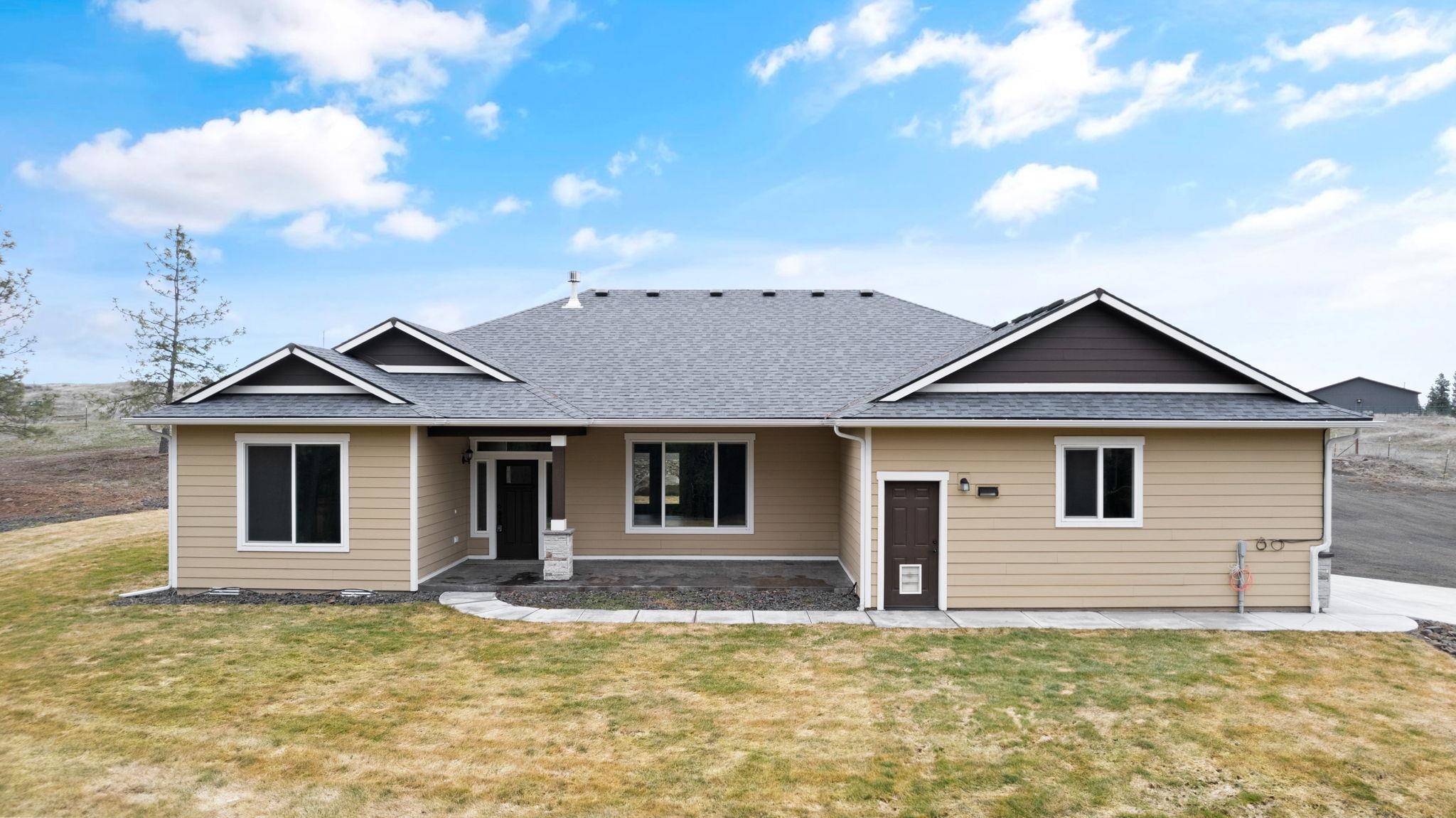 Single-story beige house with a gray gabled roof and covered front entry.