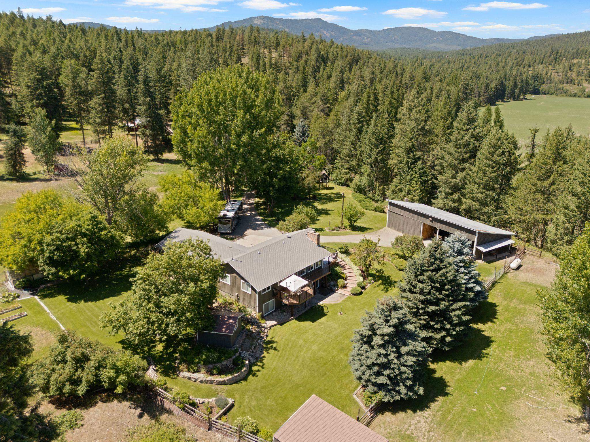 Aerial view of a country home and detached barn amid lawns and wooded mountain scenery.