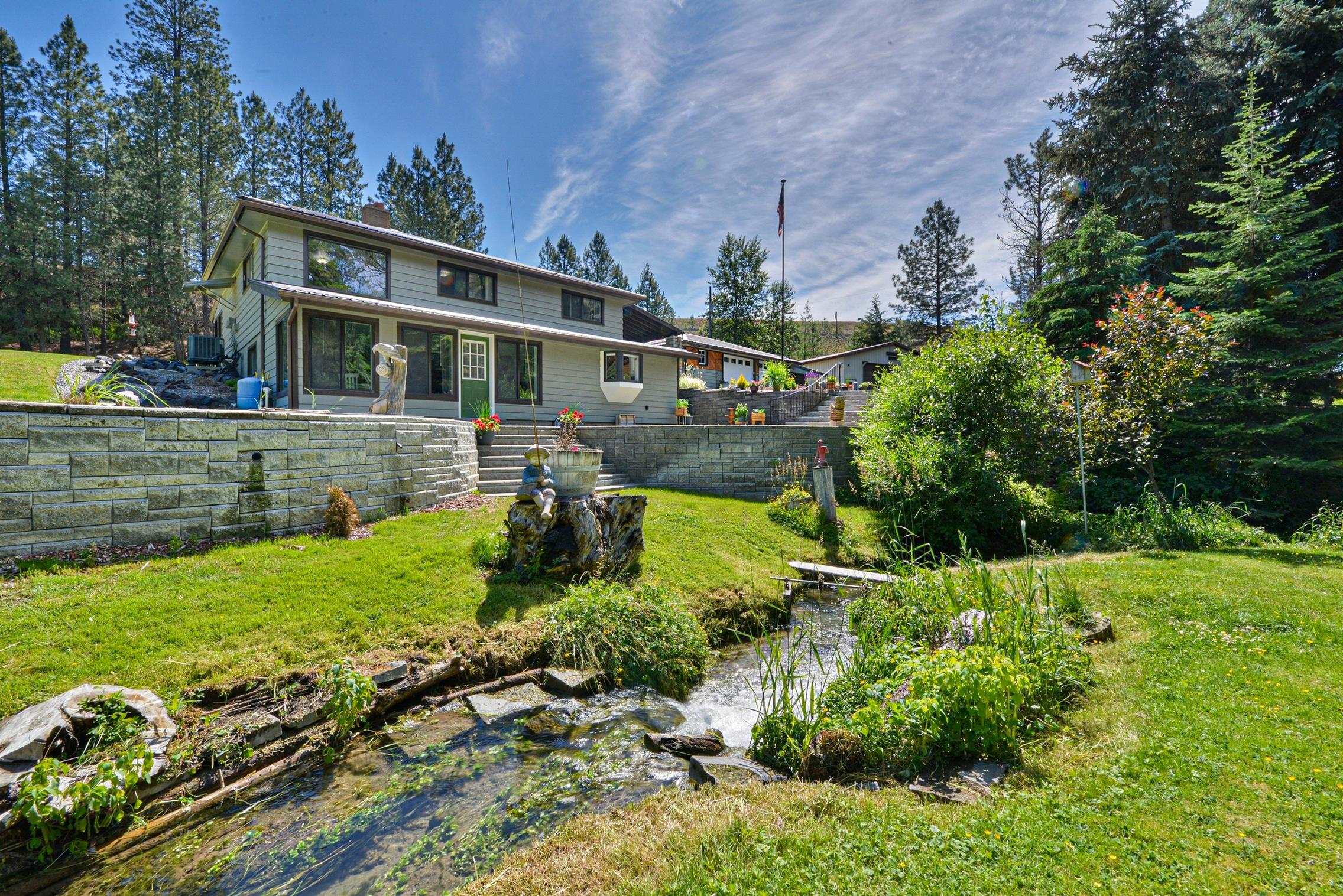 Two-story house above a landscaped yard with stone retaining walls and a small stream.