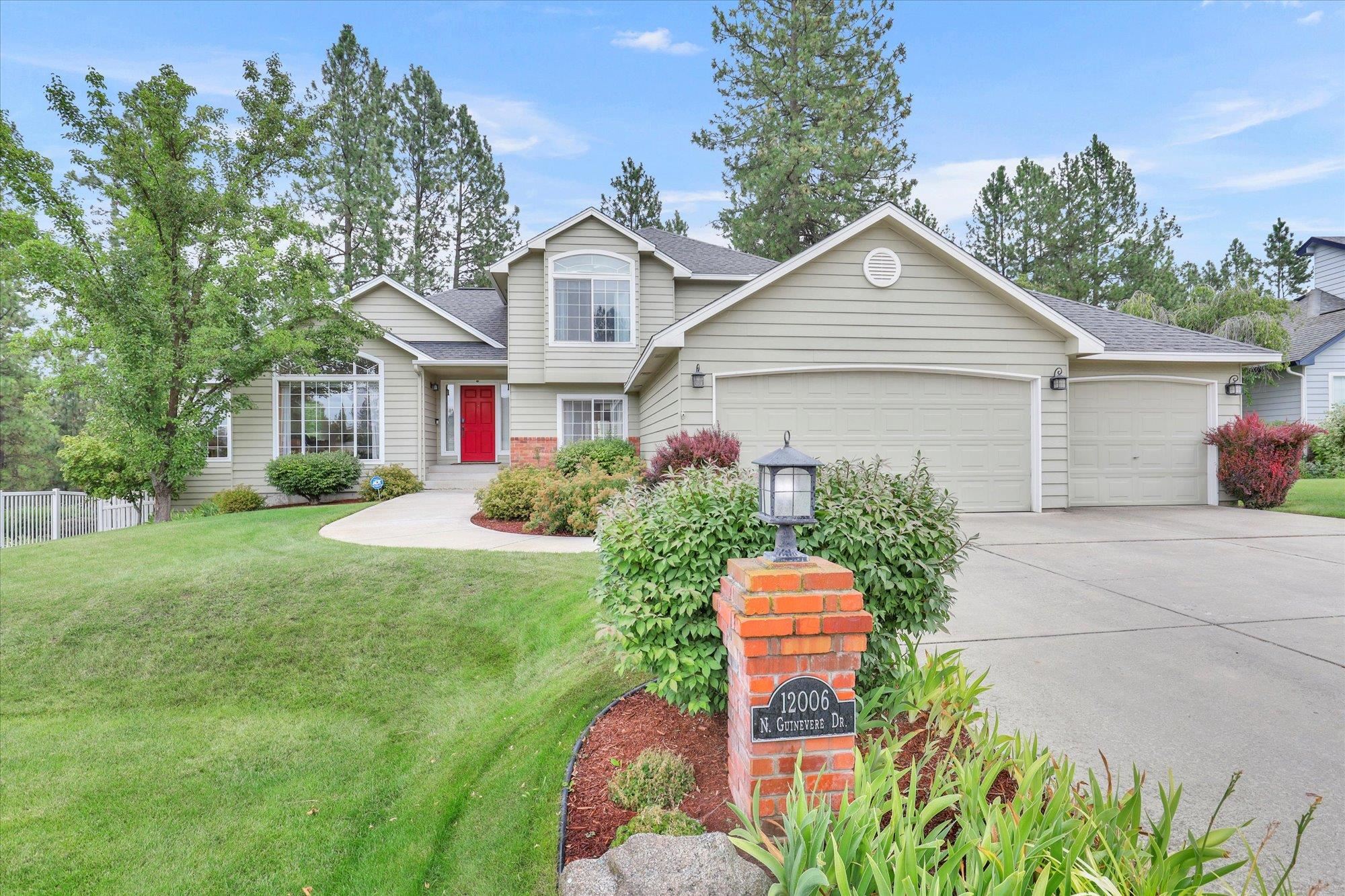 Two-story beige house with a red front door, three-car garage, and landscaped lawn.