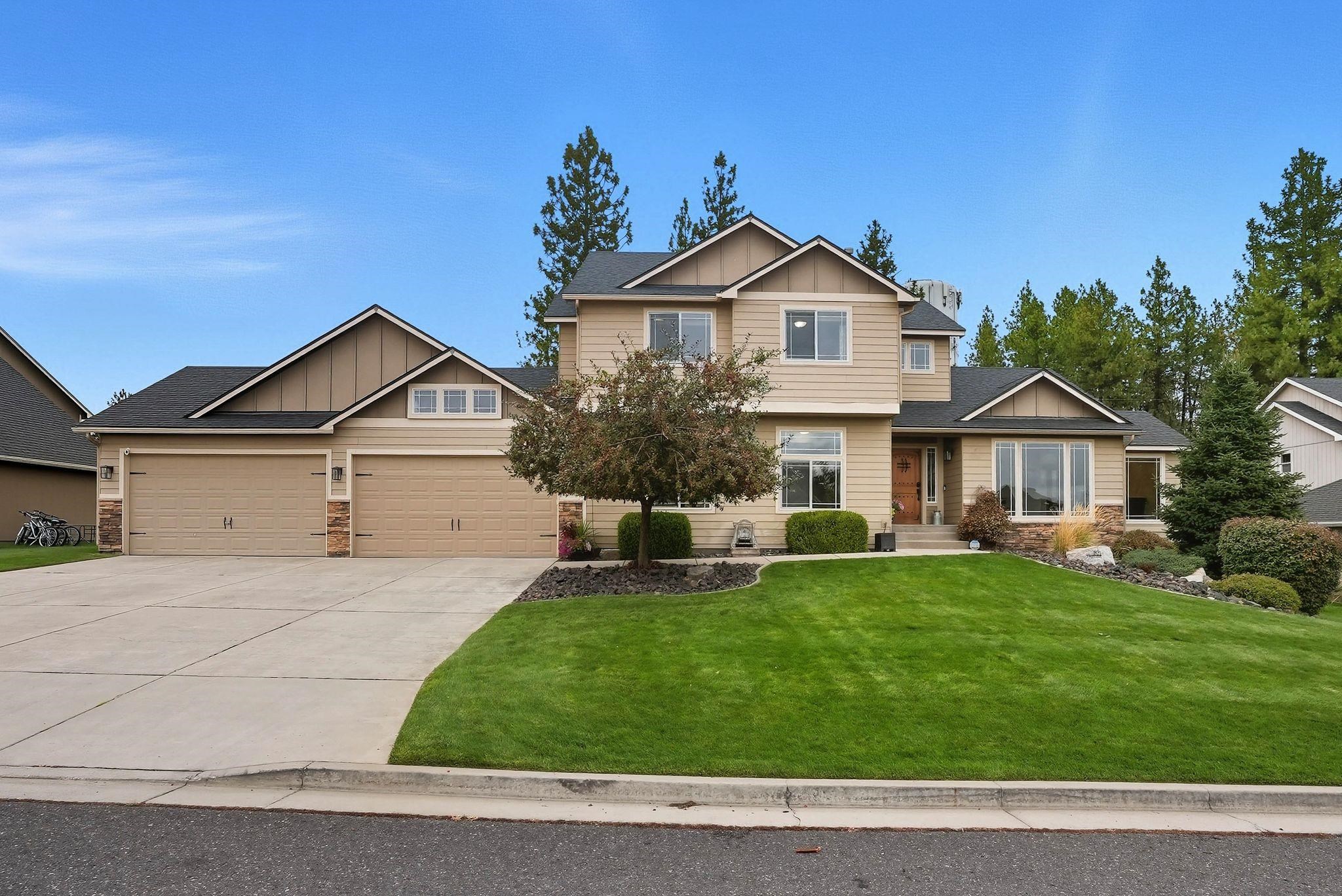 Two-story beige house with a double garage, broad driveway, and landscaped front lawn.