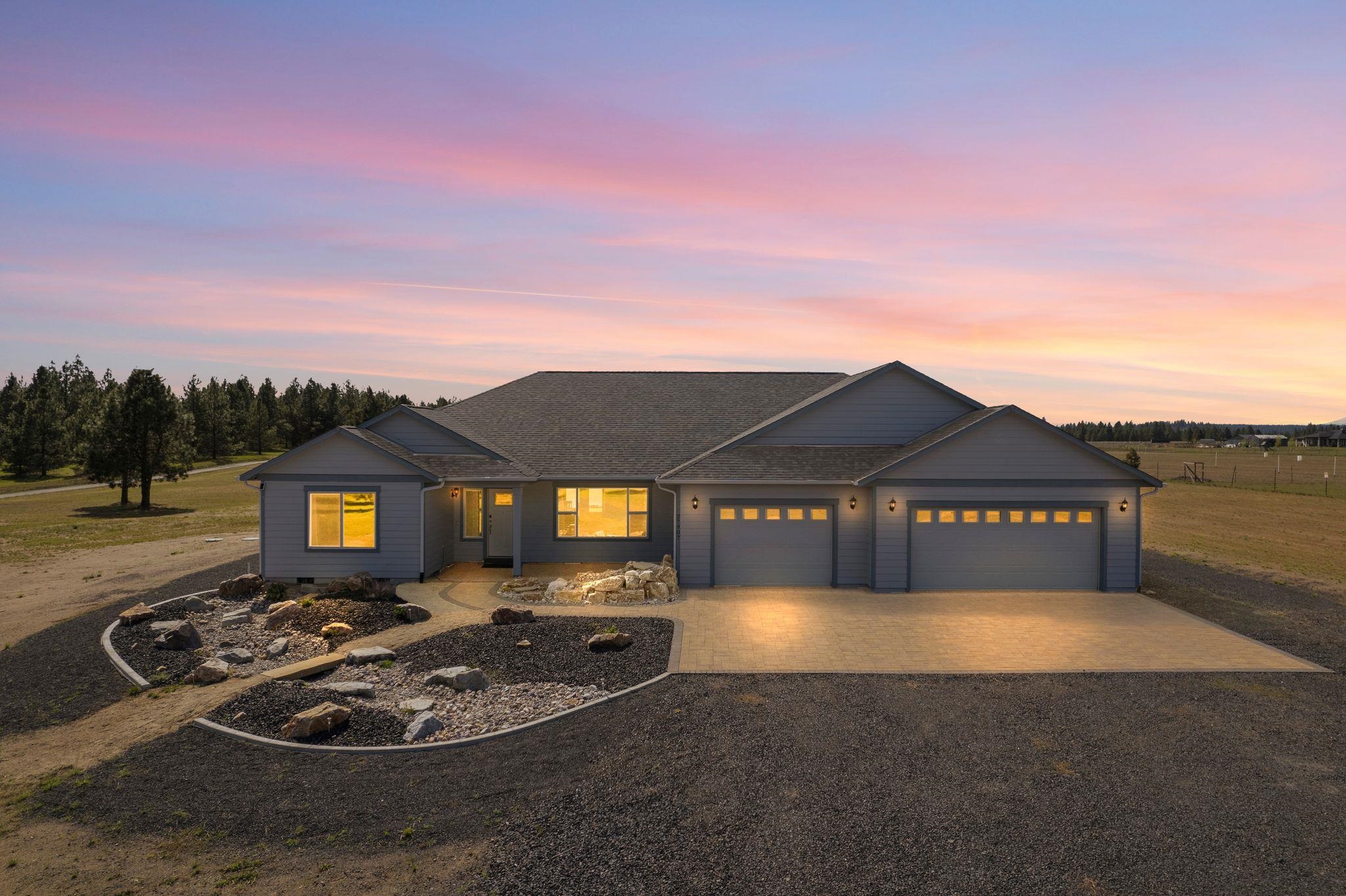 Gray single-story home with two garage doors and rock landscaping beneath a pink sunset sky.
