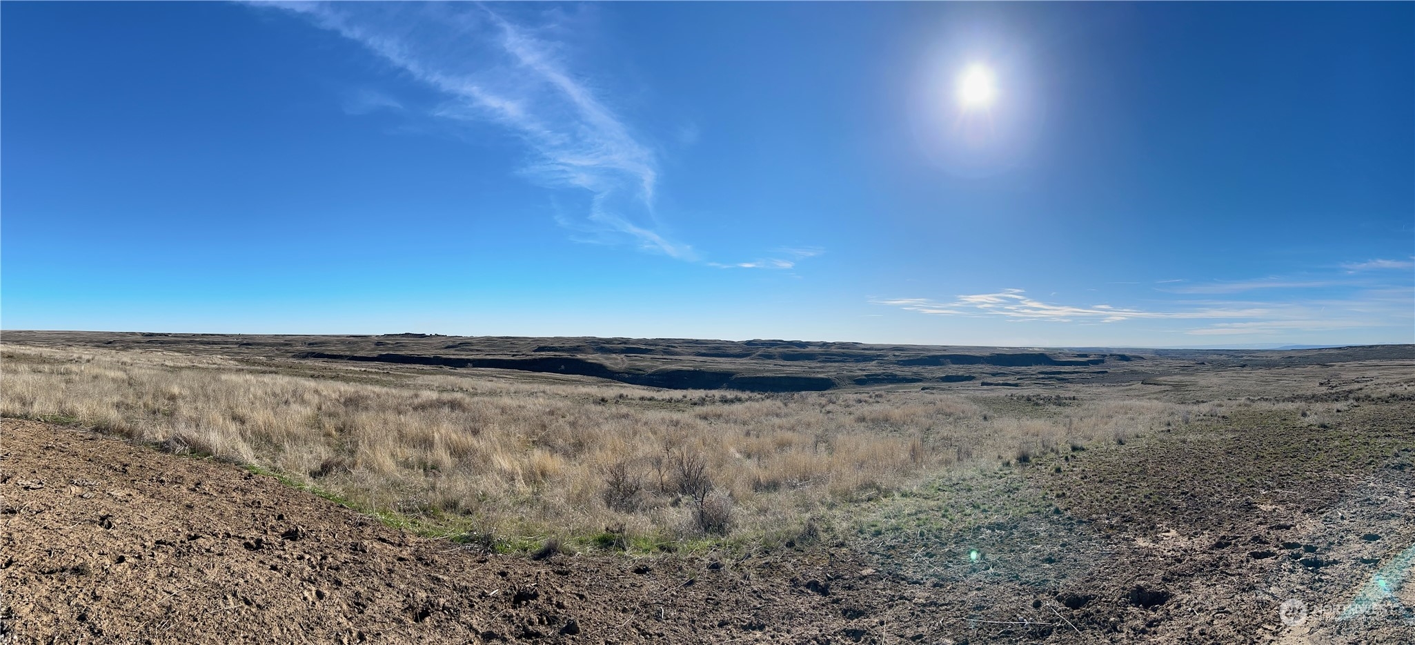 Vacant rural lot with dry grass and rolling open terrain beneath a wide blue sky.